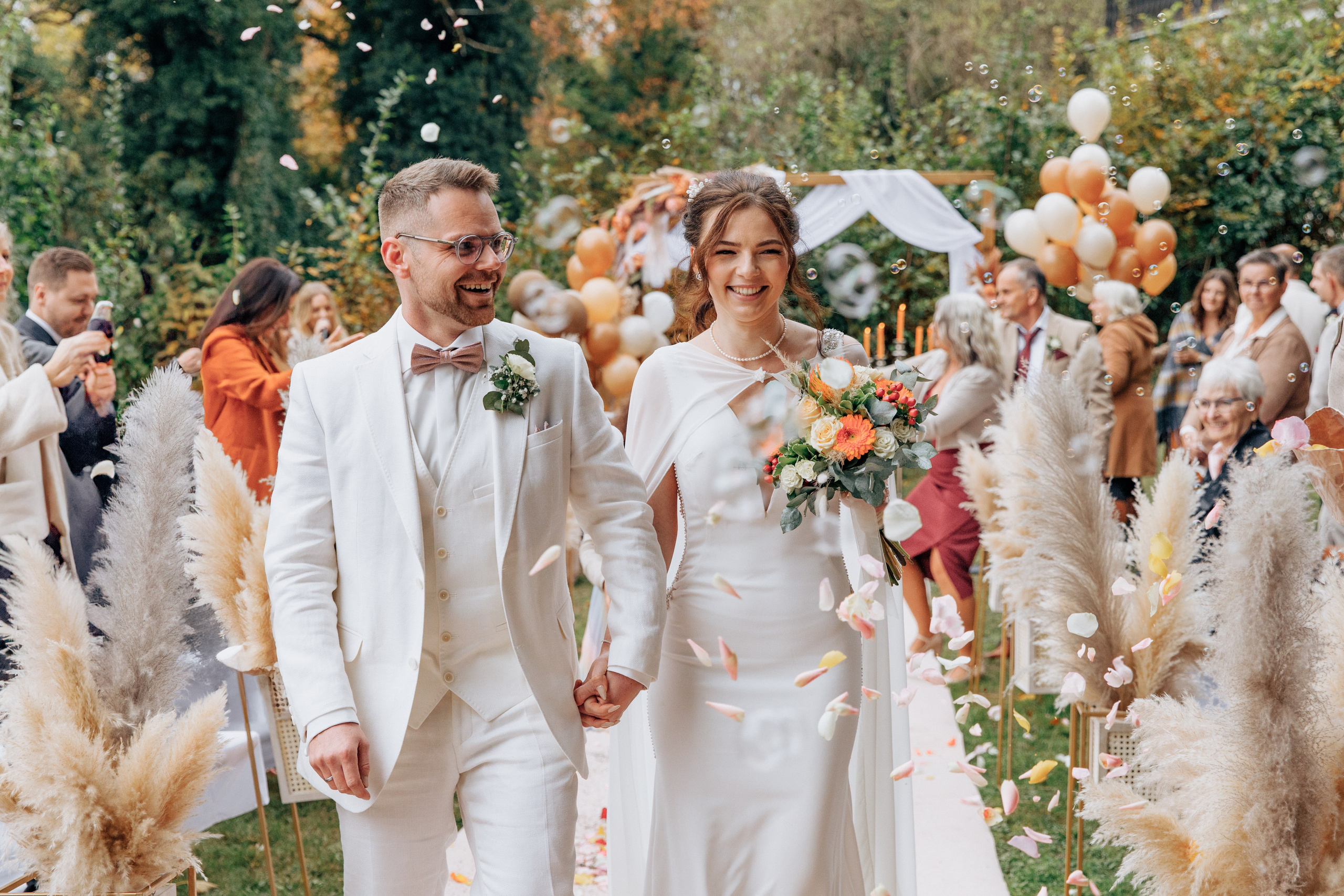 Der Bräutigam und die Braut lachen, während die Gäste sie mit Blütenblättern bewerfen