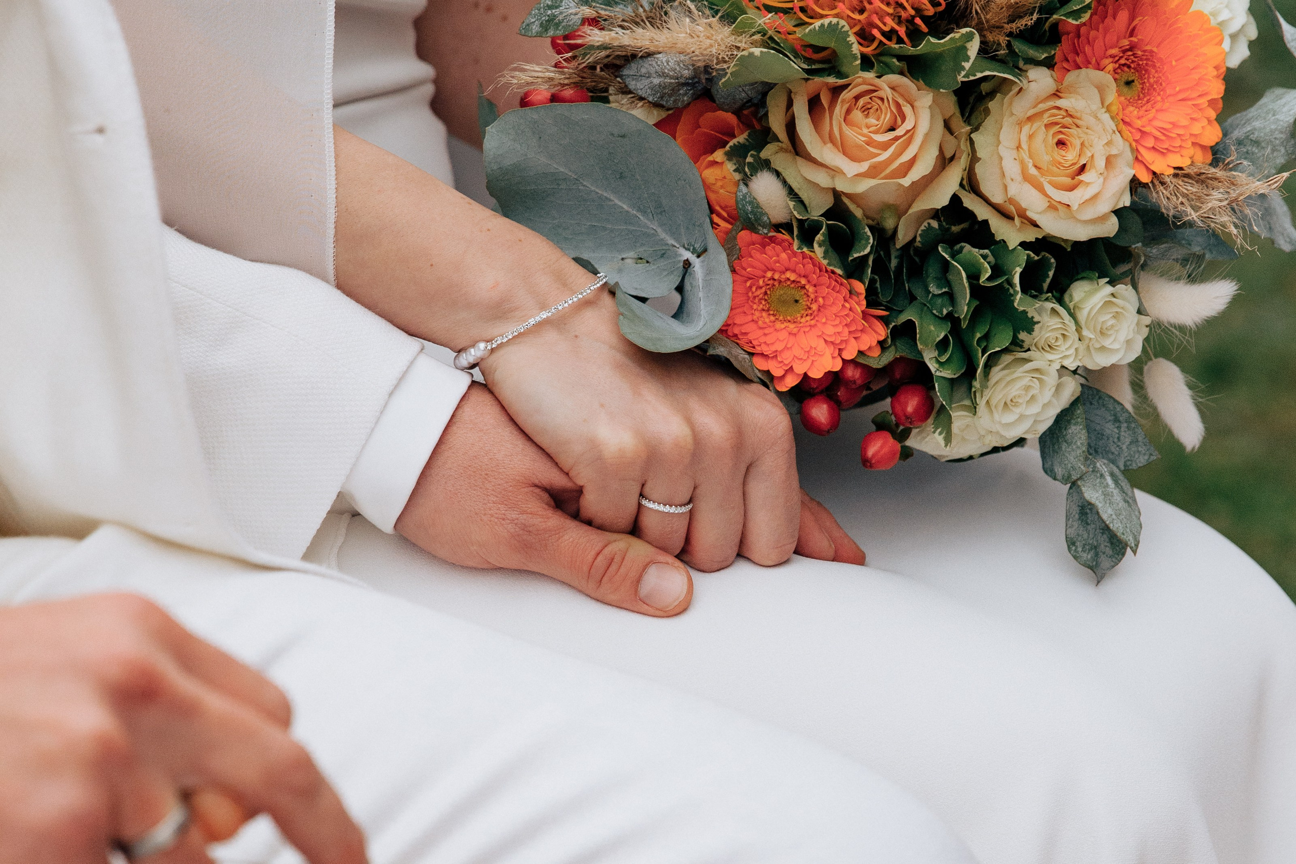 Die Braut hält die Hand des Bräutigams und ihr schöner Ehering ist sichtbar.