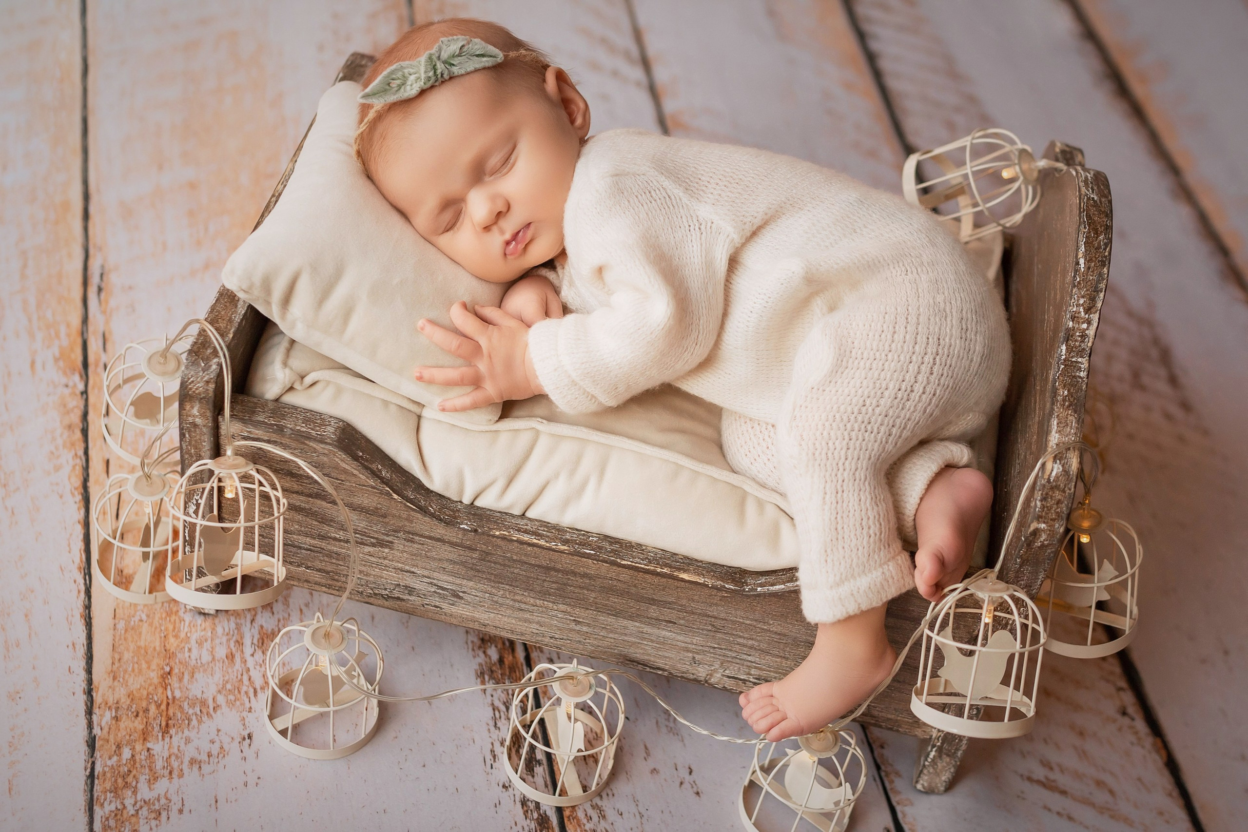 Newborn baby girl sleeping on side in wooden crib, head on pillow