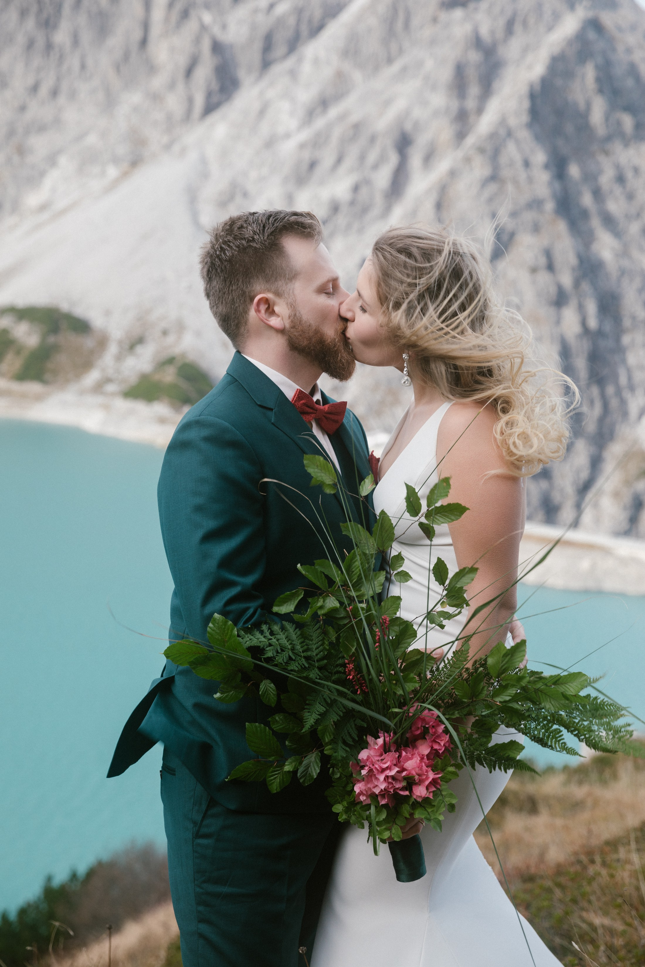 Nahaufnahme Hochzeitskuss mit Strauß, türkisfarbener Bergsee im Hintergrund