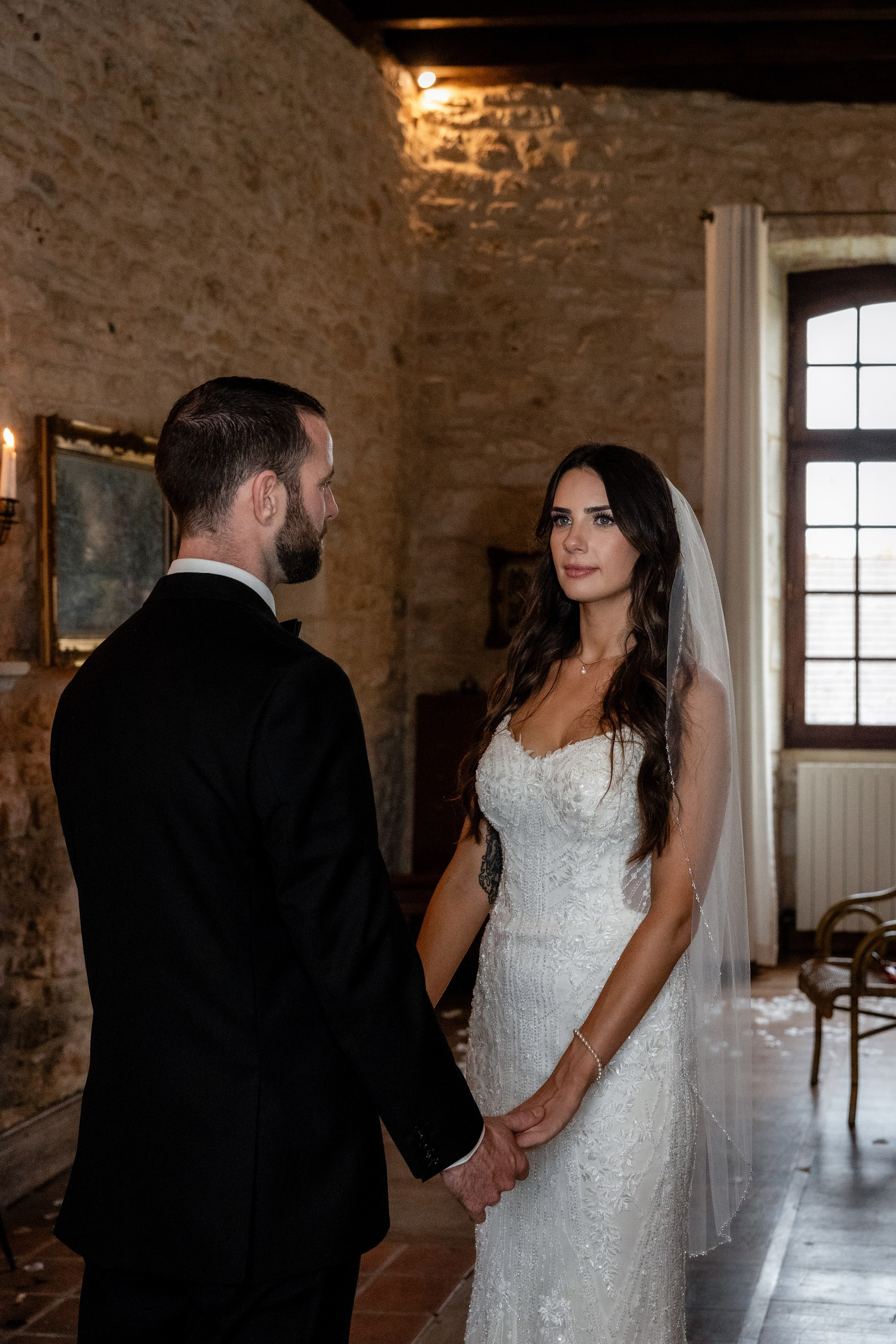 Bride and groom holding hands through the window – emotional first touch at Château Lagut.