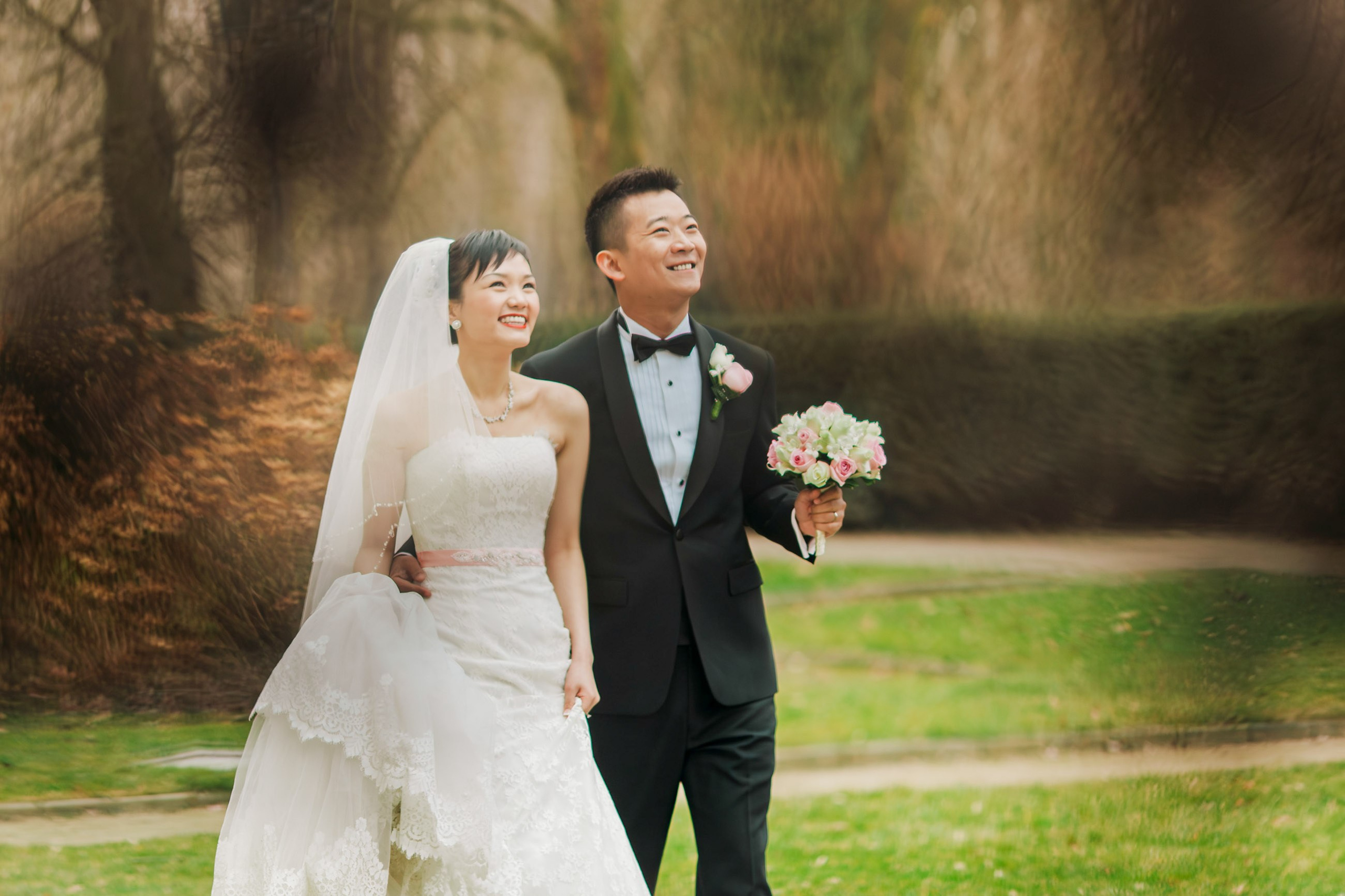 A smling Hong Kong bride and her tuxedo wearing groom walk across the winter landscape of the historic Castle Hluboka during their destination wedding in Czechia.