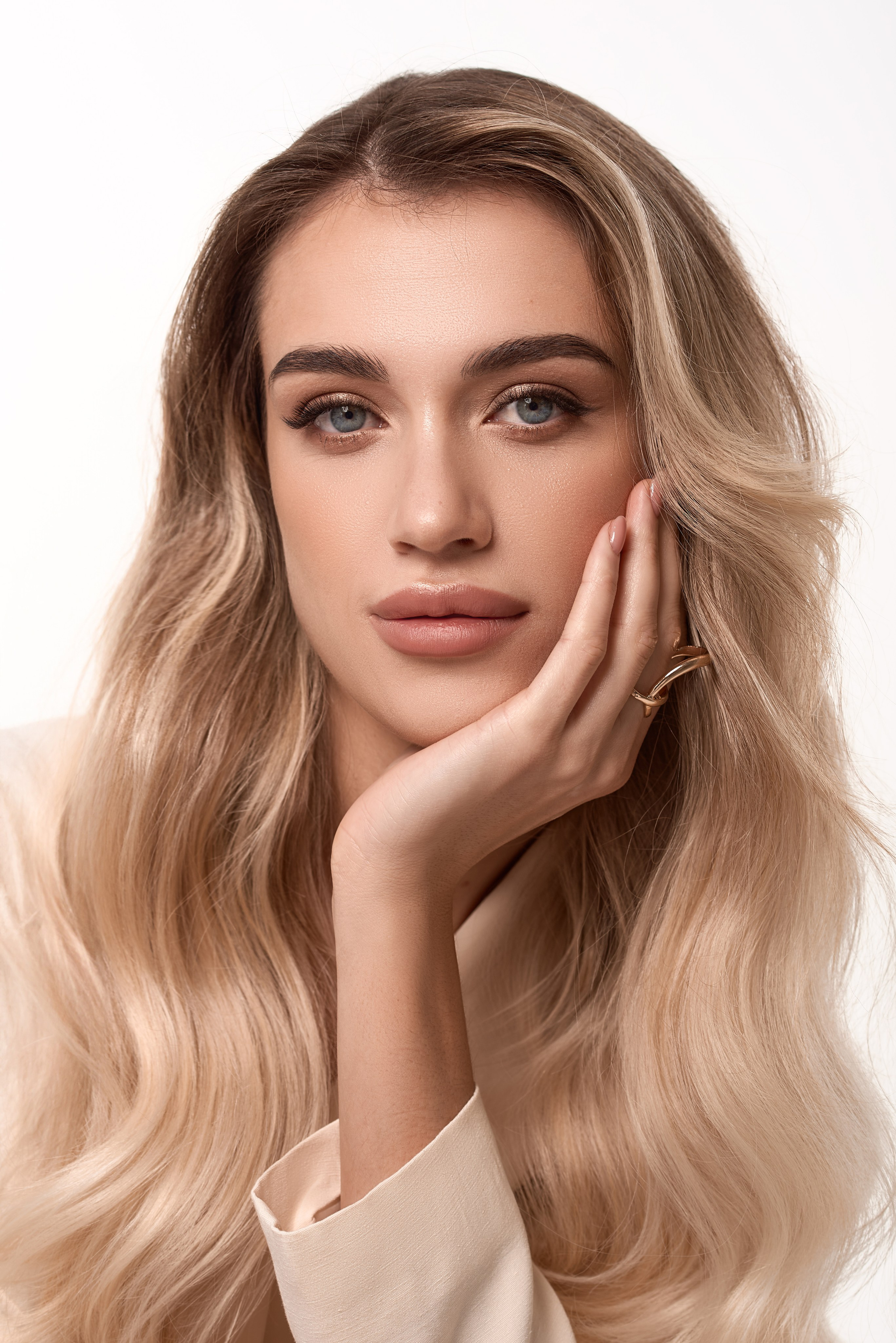 Крупний план обличчя жінки з виразними блакитними очима. Вона легко спирається рукою на обличчя, створюючи атмосферу ніжності та задумливості.