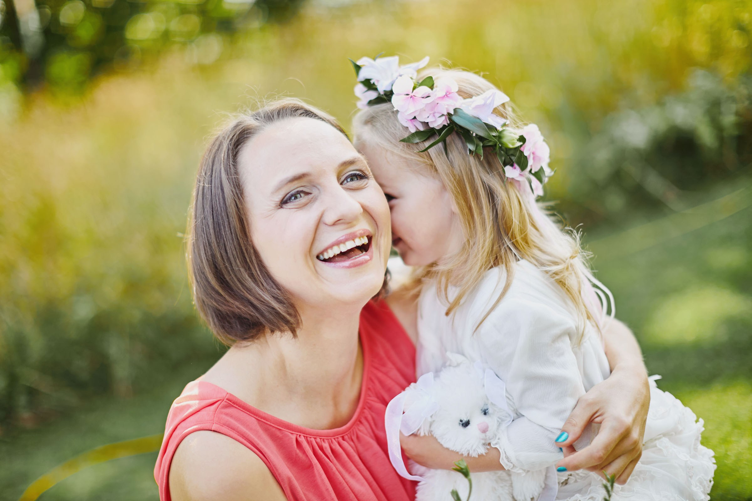 Shy flower girl cuddling mother post-run at start of outdoor wedding.