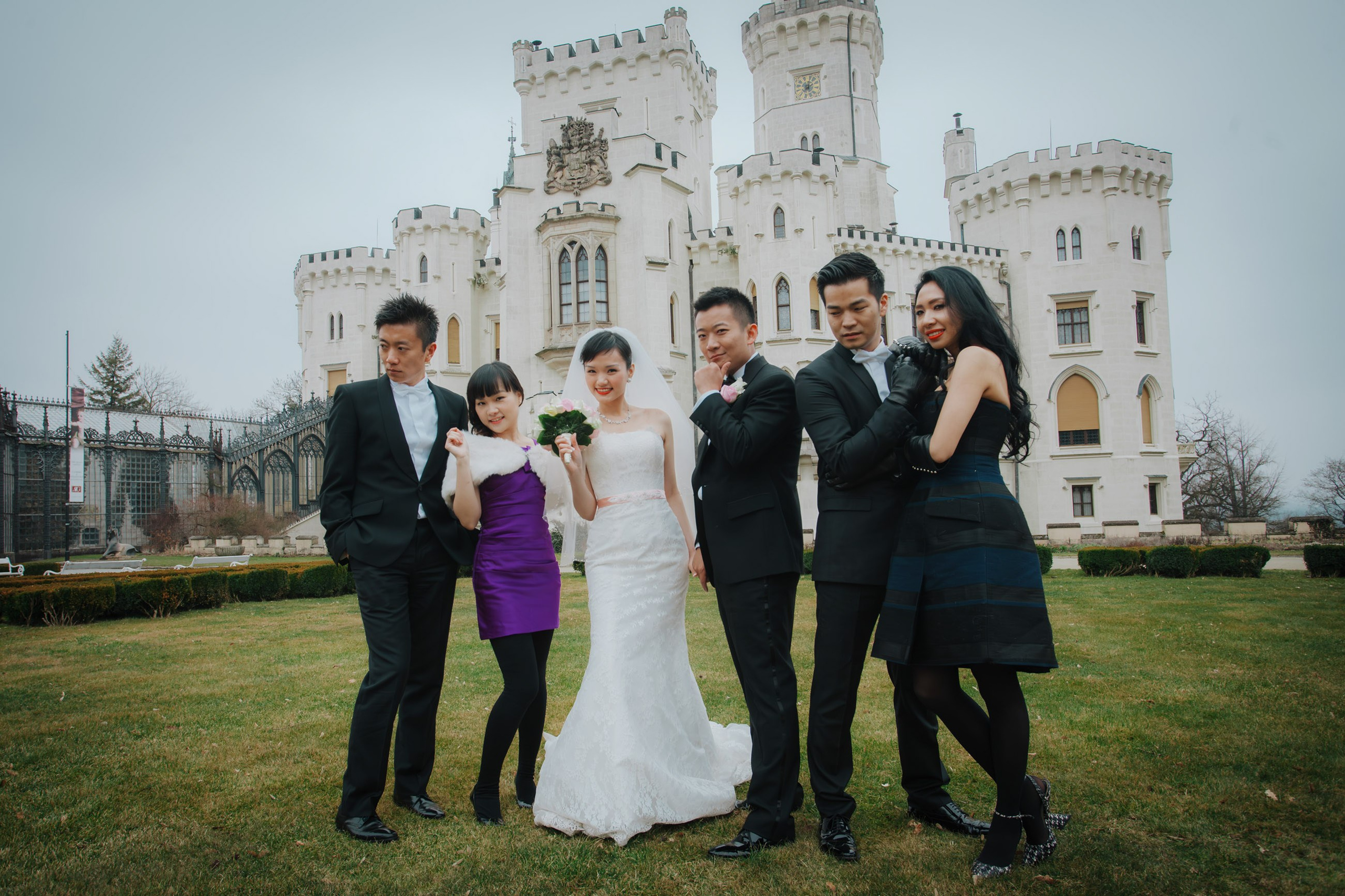 A Hong Kong bride and groom are surrounded by their close friends as they make a funny face on the grounds of the State Chateau of Hluboka during their destination wedding in Czechia.