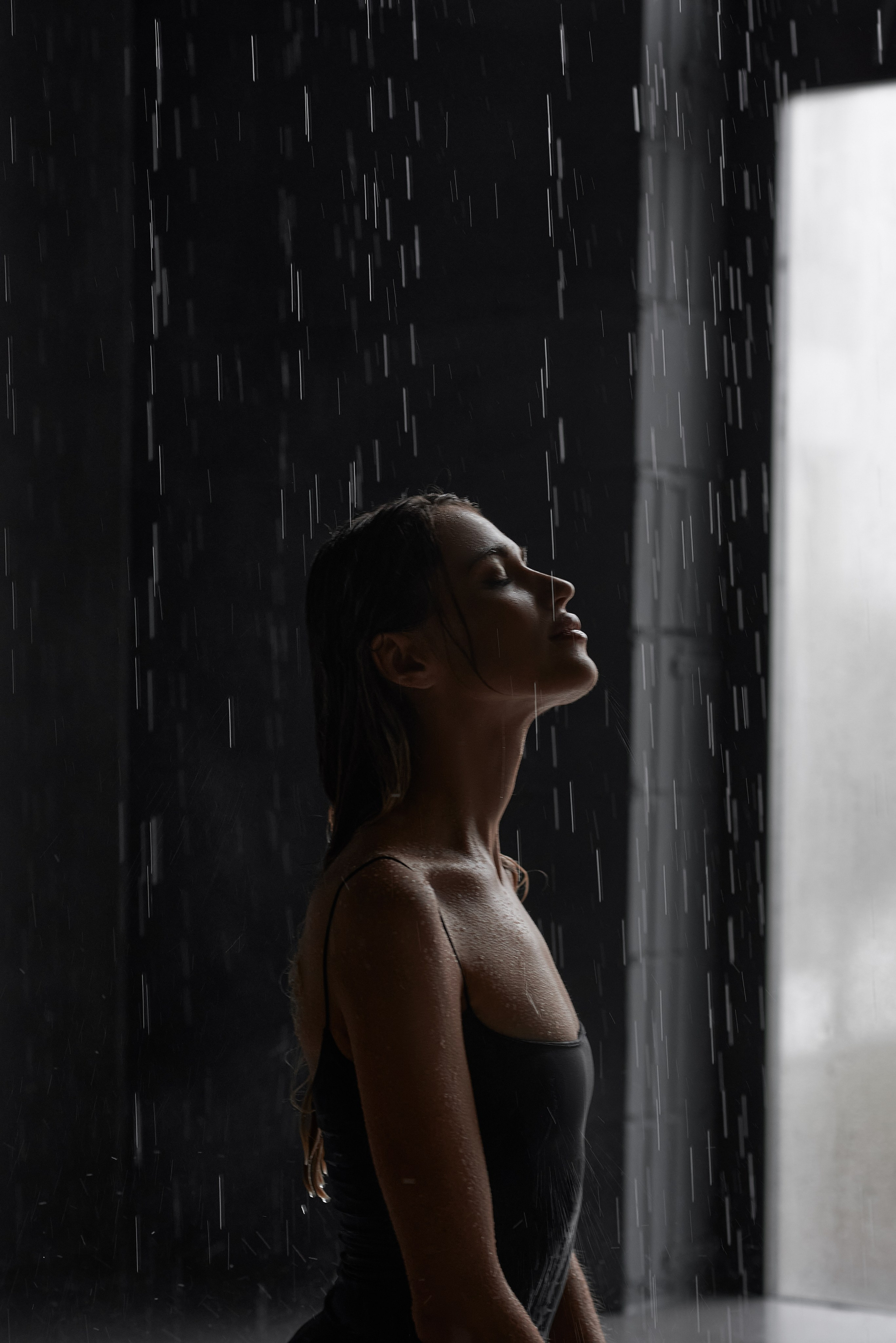 Чуттєва студійна фотосесія: жінка в чорному вбранні з мокрим ефектом позує під краплями води, підкреслюючи природну красу.