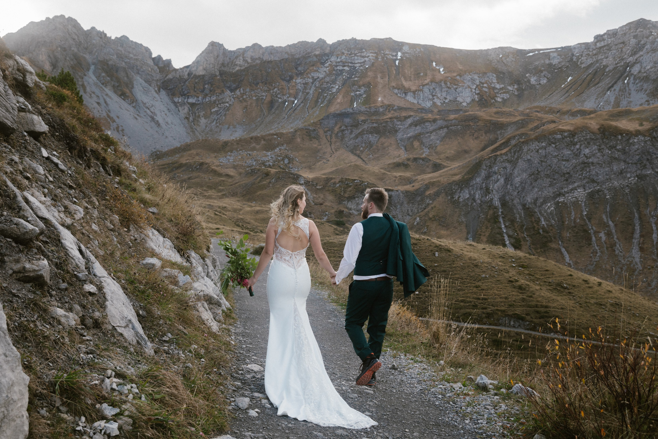 Brautpaar Hand in Hand auf steinigem Alpenweg bei Fotosession