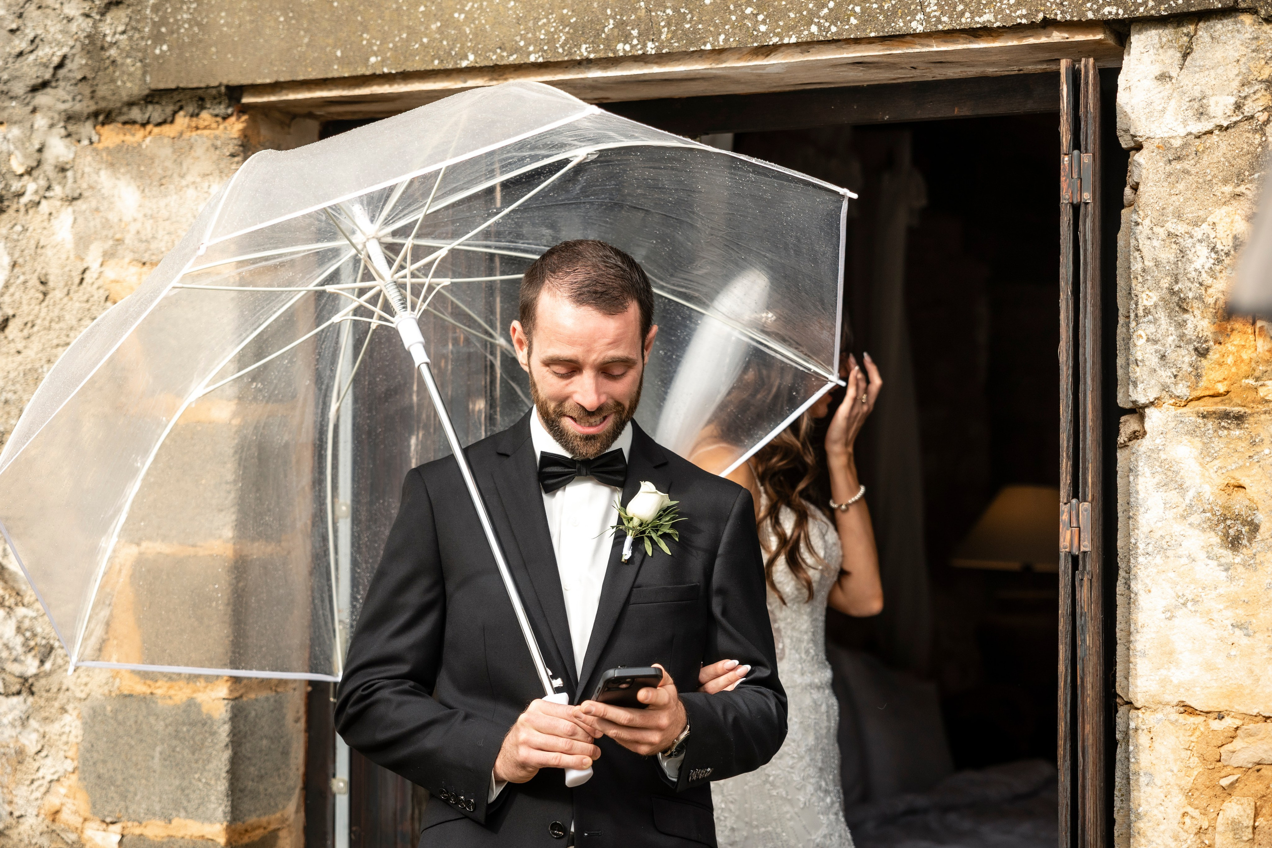 Groom standing under umbrella during rainy wedding in Dordogne, France.