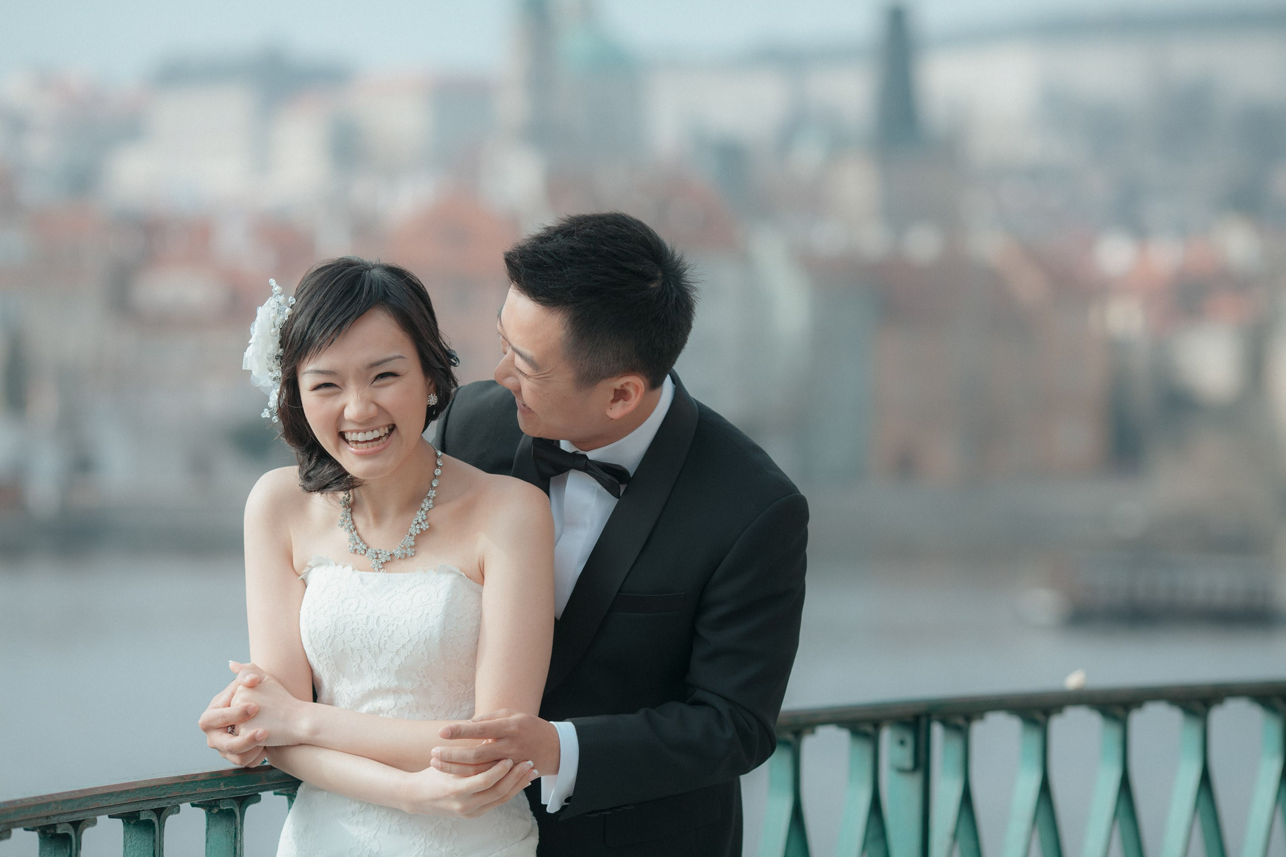 The beaming couple from Hong Kong share a laugh as they cuddle near the riverside in Prague during their pre-wedding photo session.