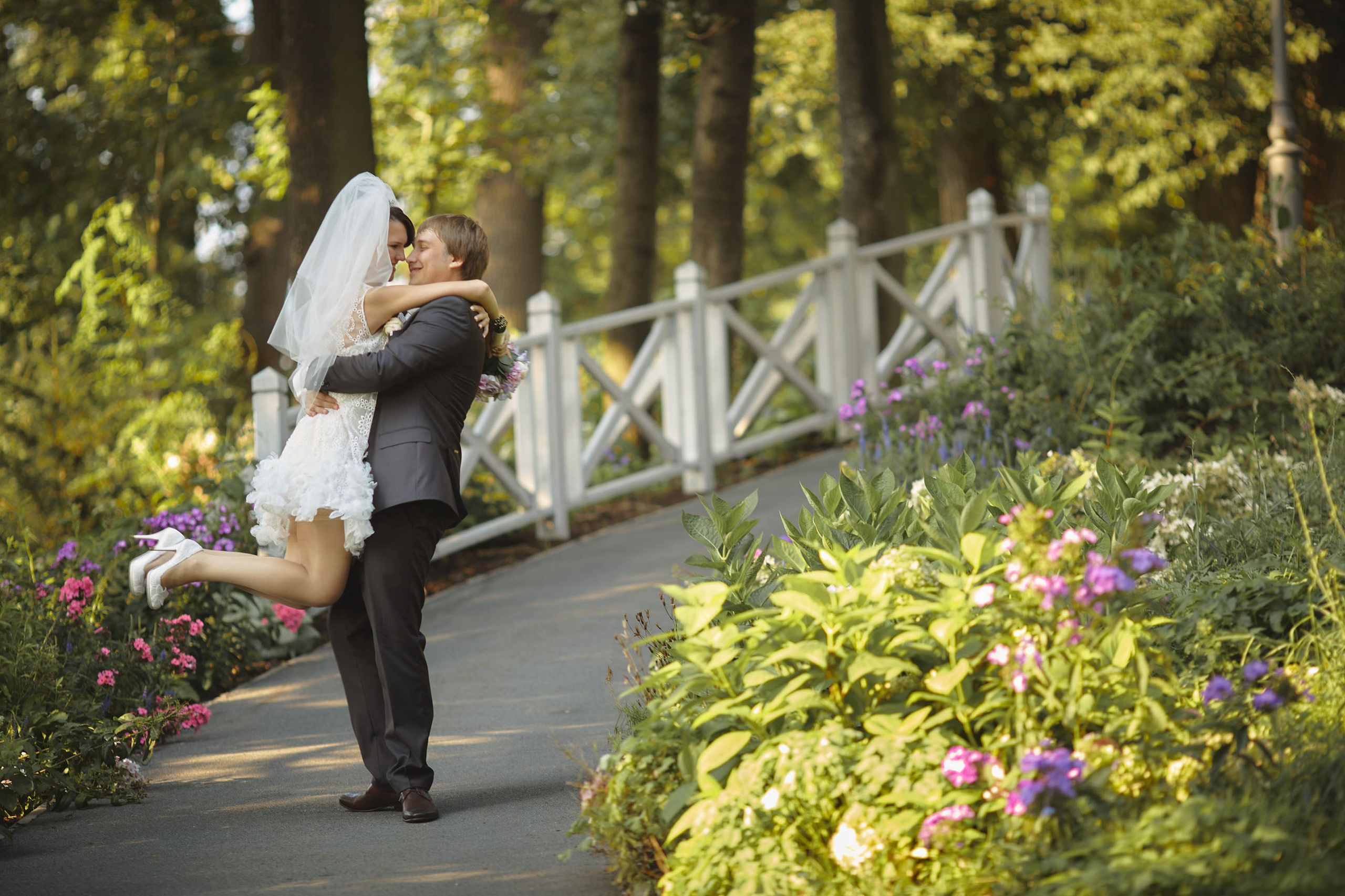 A groom kisses his bride after picking her up amidst the vibrant garden landscapes of Chateau Mcely, celebrating their magical wedding ceremony.