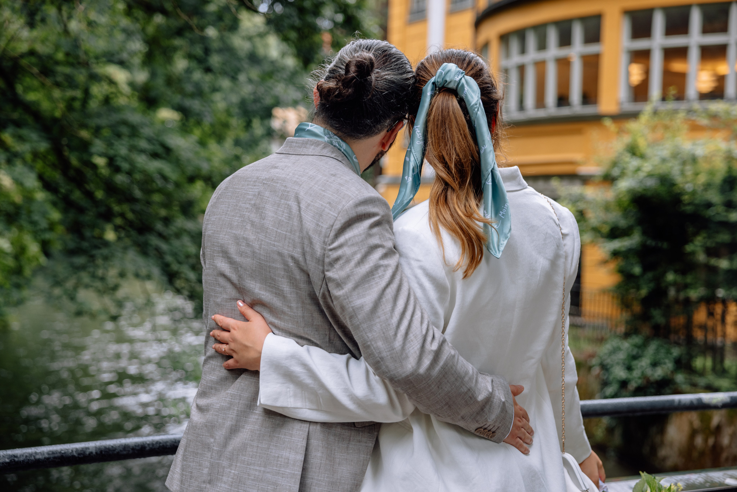 Braut und Bräutigam schauen in die Ferne – romantische Szene am Wasser, Standesamt Mandlstraße 14 im Hintergrund