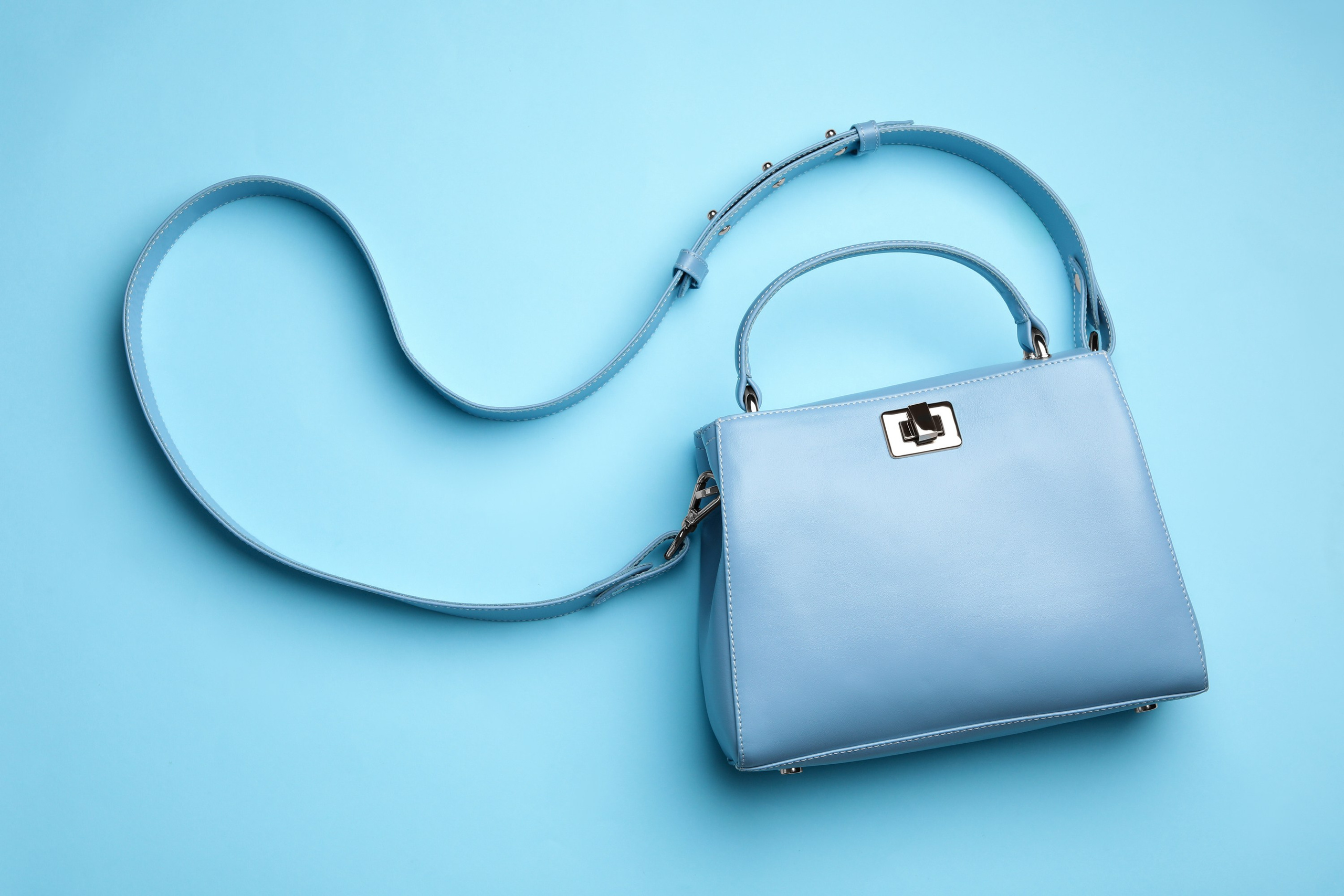 Light blue handbag with a long strap on a matching blue background