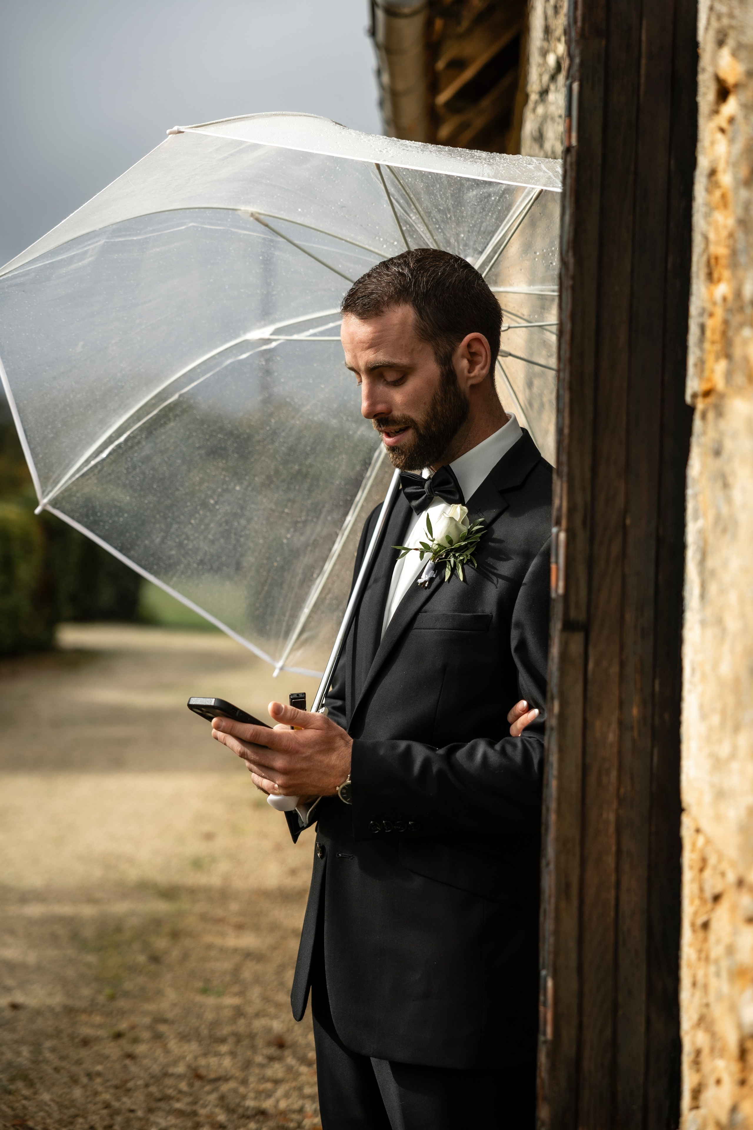Groom standing under umbrella during rainy wedding in Dordogne, France.