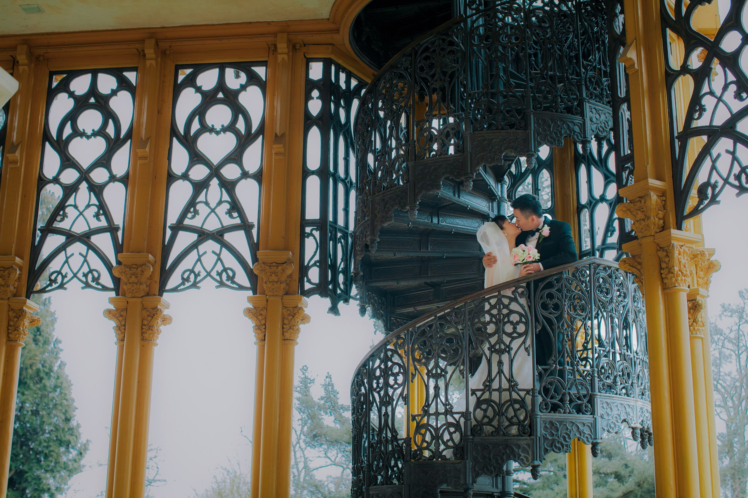 A smiling Hong Kong bride and groom pose for a photo on the historic staircase on the grounds of the State Chateau of Hluboka during their destination wedding in Bohemia.