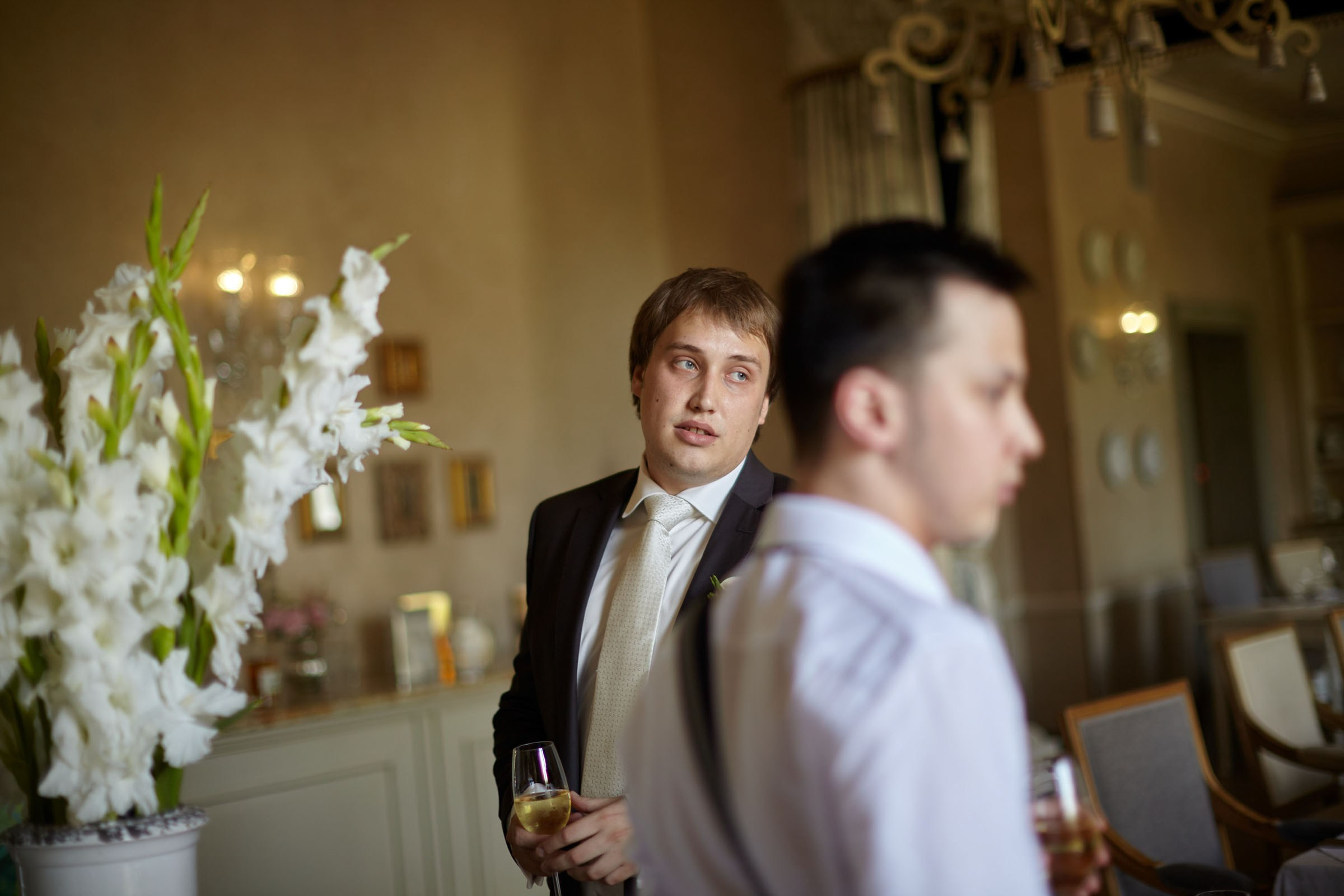 Nervous groom with wine glass looking out window at Chateau Mcely wedding prep.