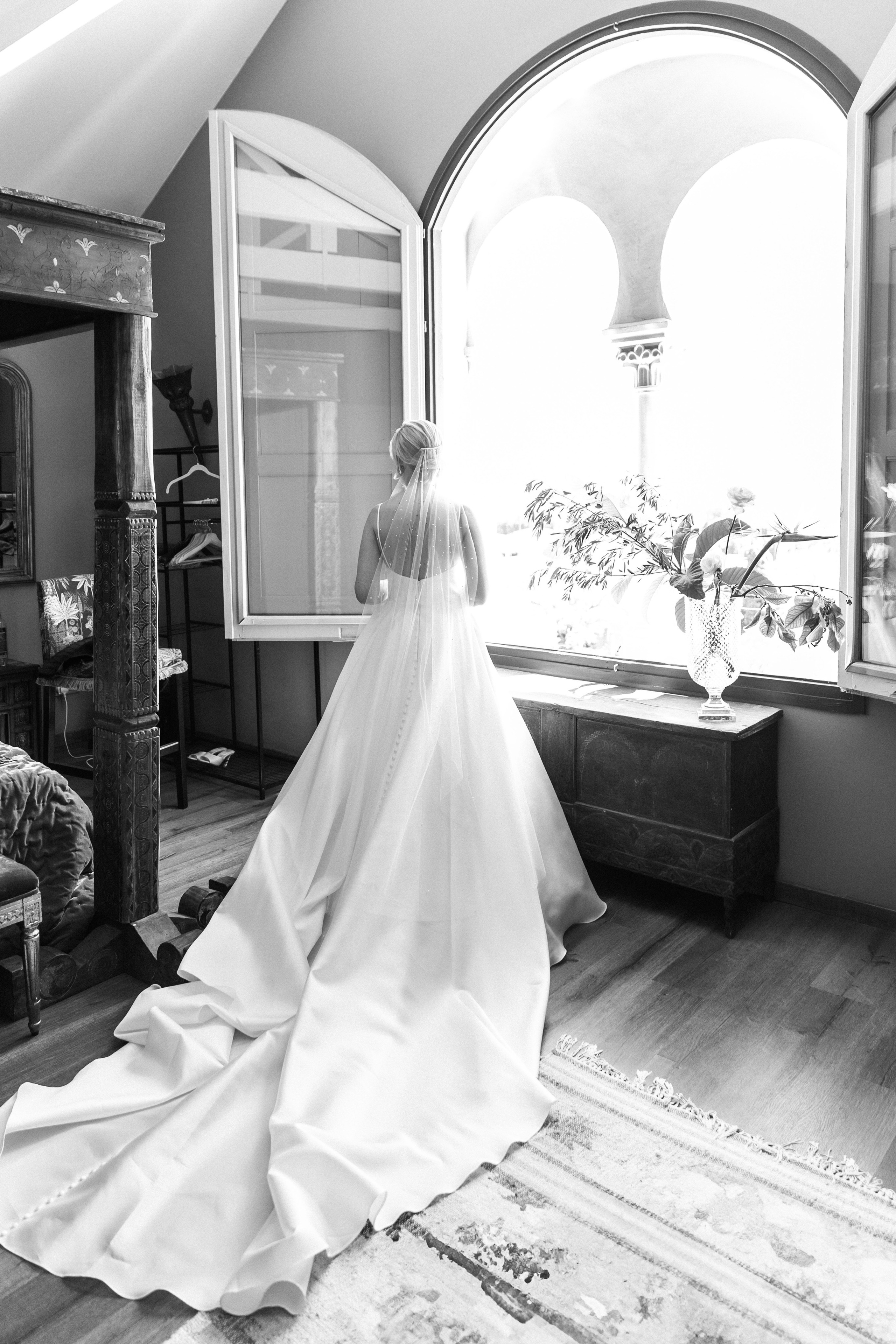 The bride is next to the window at her wedding venue in Barcelona, creating an emotional scene.