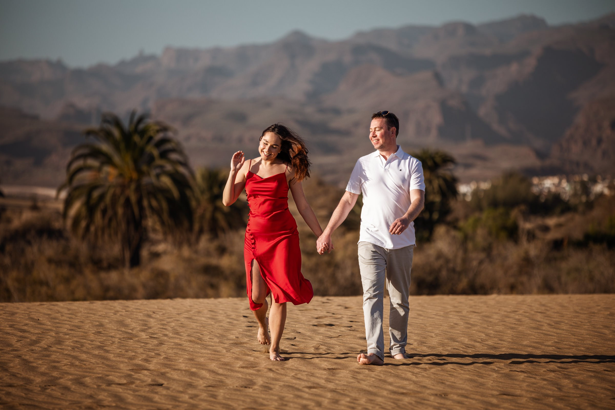 Pari kävelee hiekassa palmujen taustalla autiomaassa Dunas Maspalomasissa paikallisen valokuvaajan kanssa