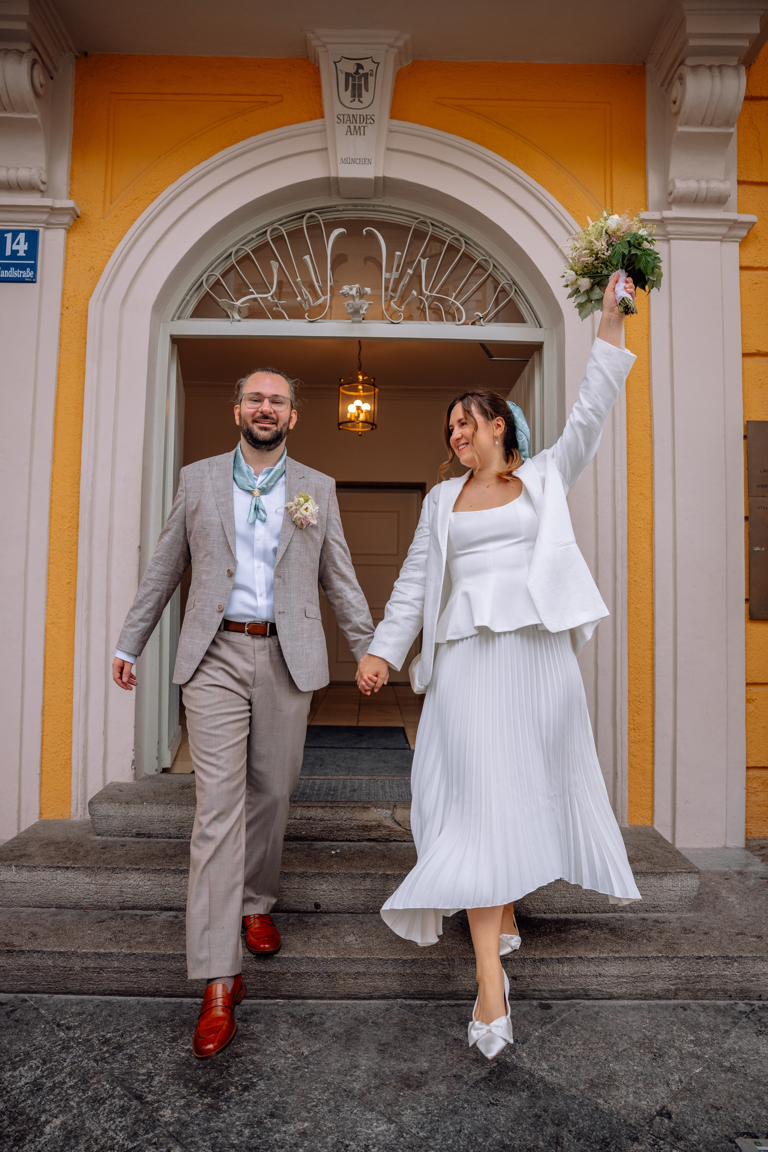 Bräutigam hält Braut an der Hand – hilft ihr die Treppe des Standesamts hinunter.