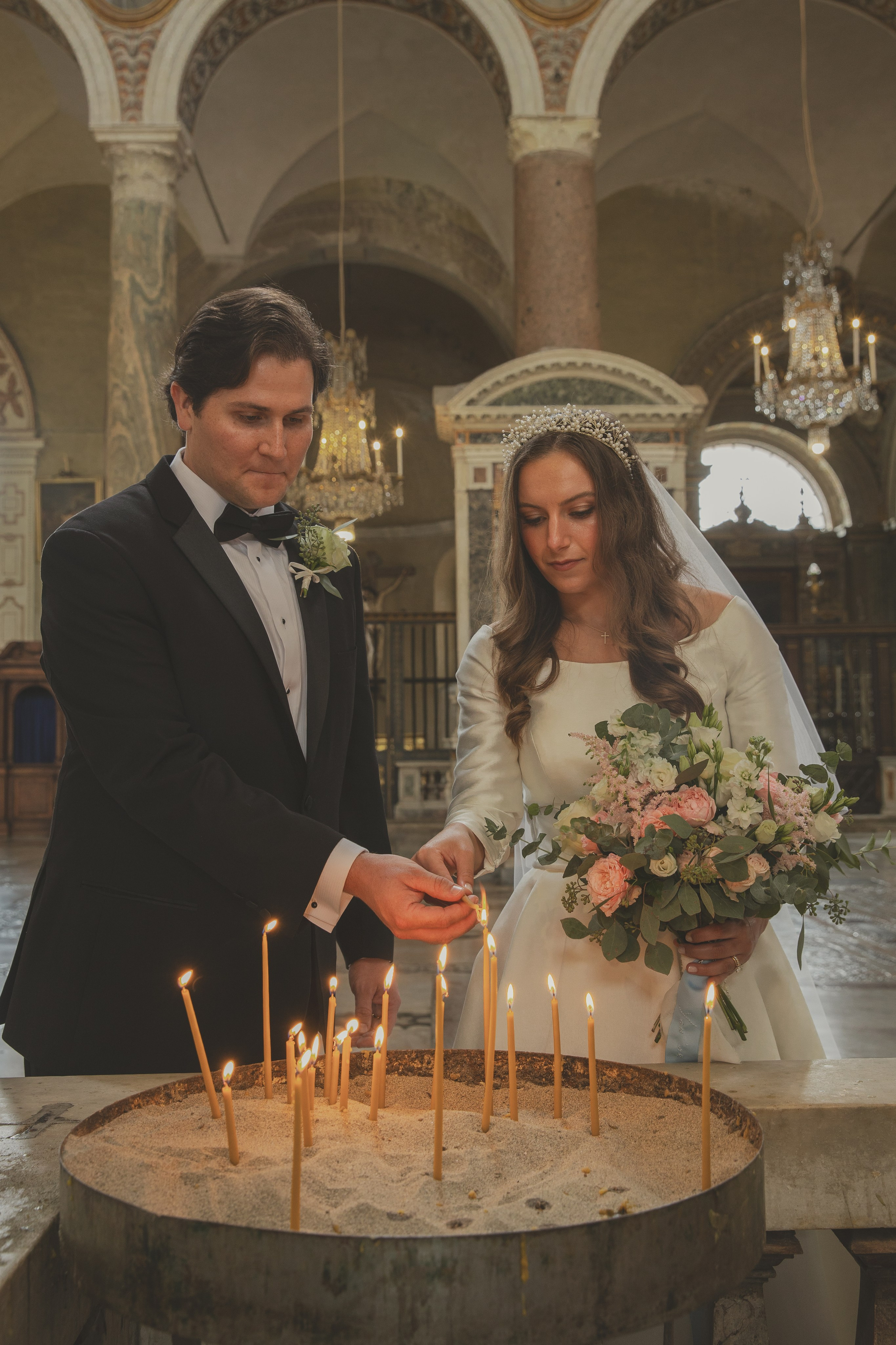 Couple lighting candles next to the icon of the Virgin Mary during their wedding ceremony.