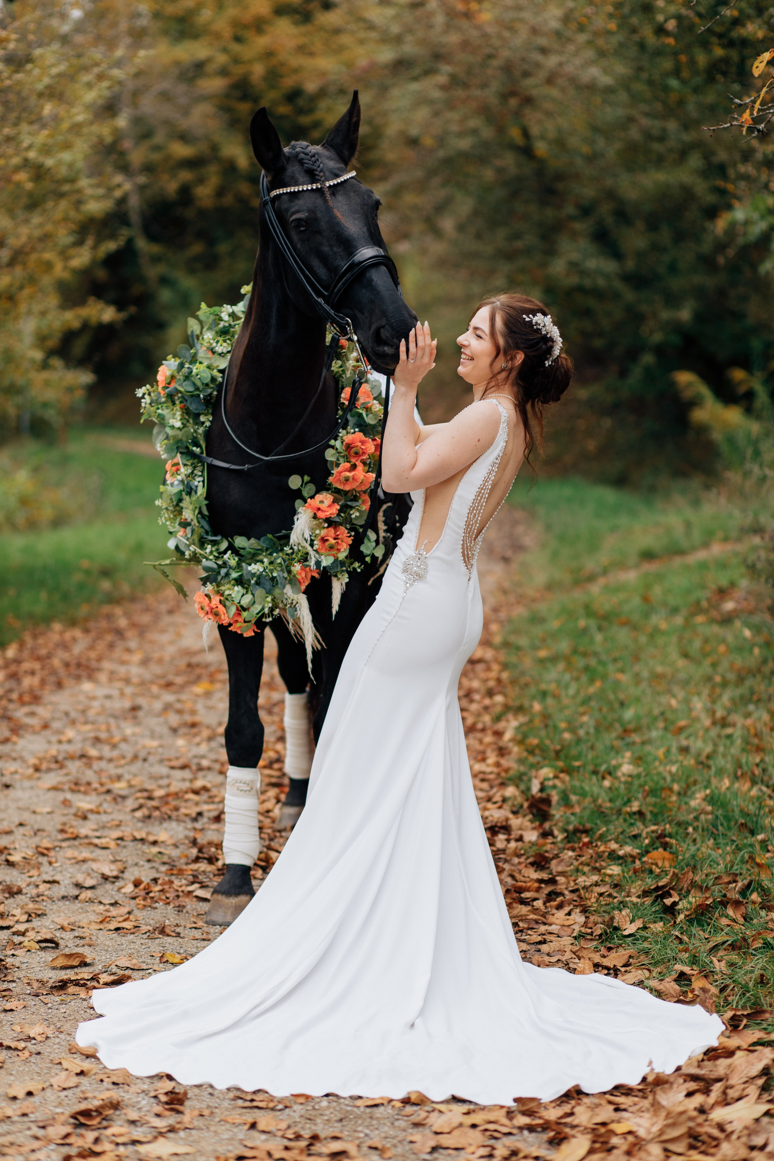 Die Braut umarmt das Pferd und zieht sich lachend zurück, während der Schleppe ihres wunderschönen Hochzeitskleides sich über den Boden erstreckt.
