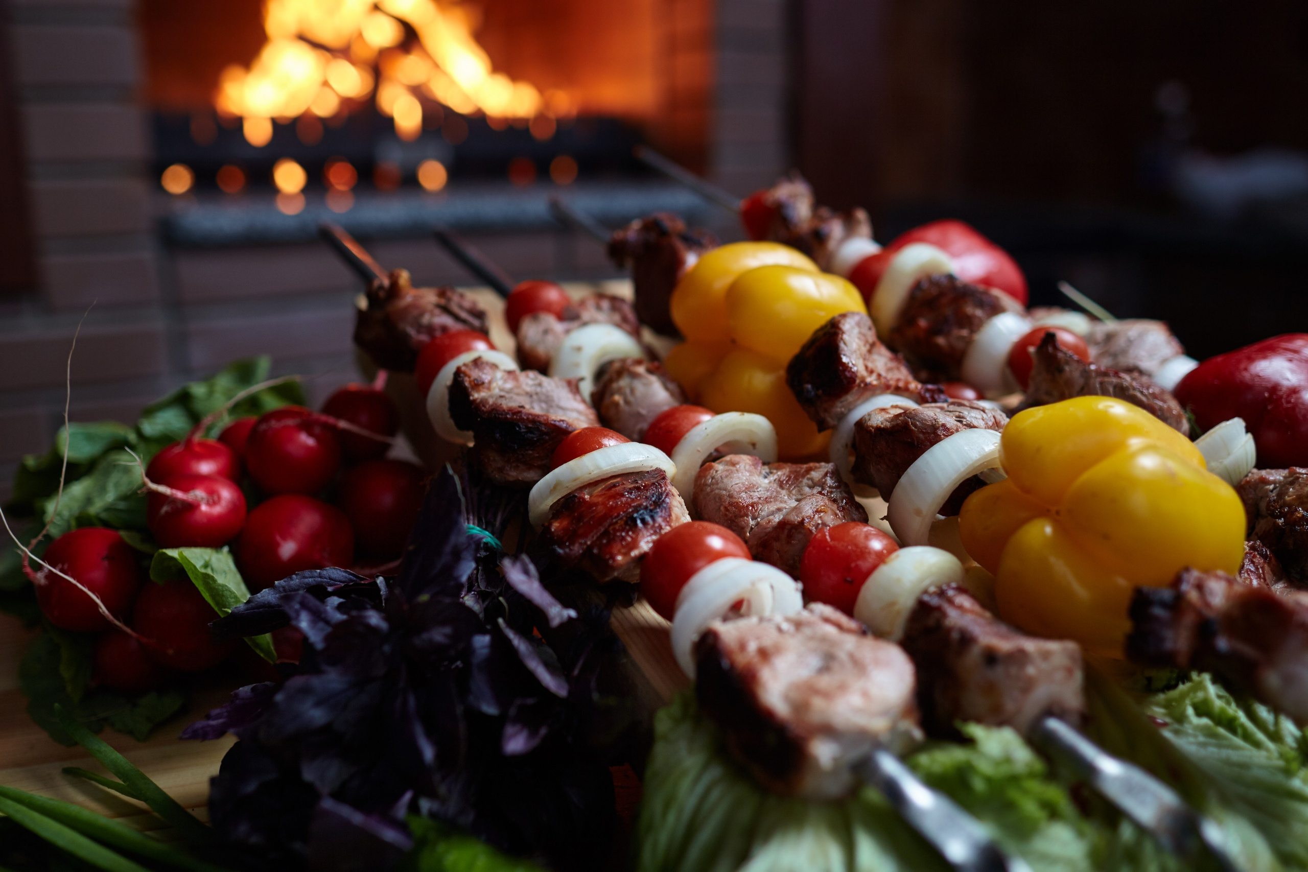 Photographie culinaire d’une planche apéritive colorée avec brochettes, agrumes et herbes fraîches – ambiance chaleureuse avec feu de cheminée