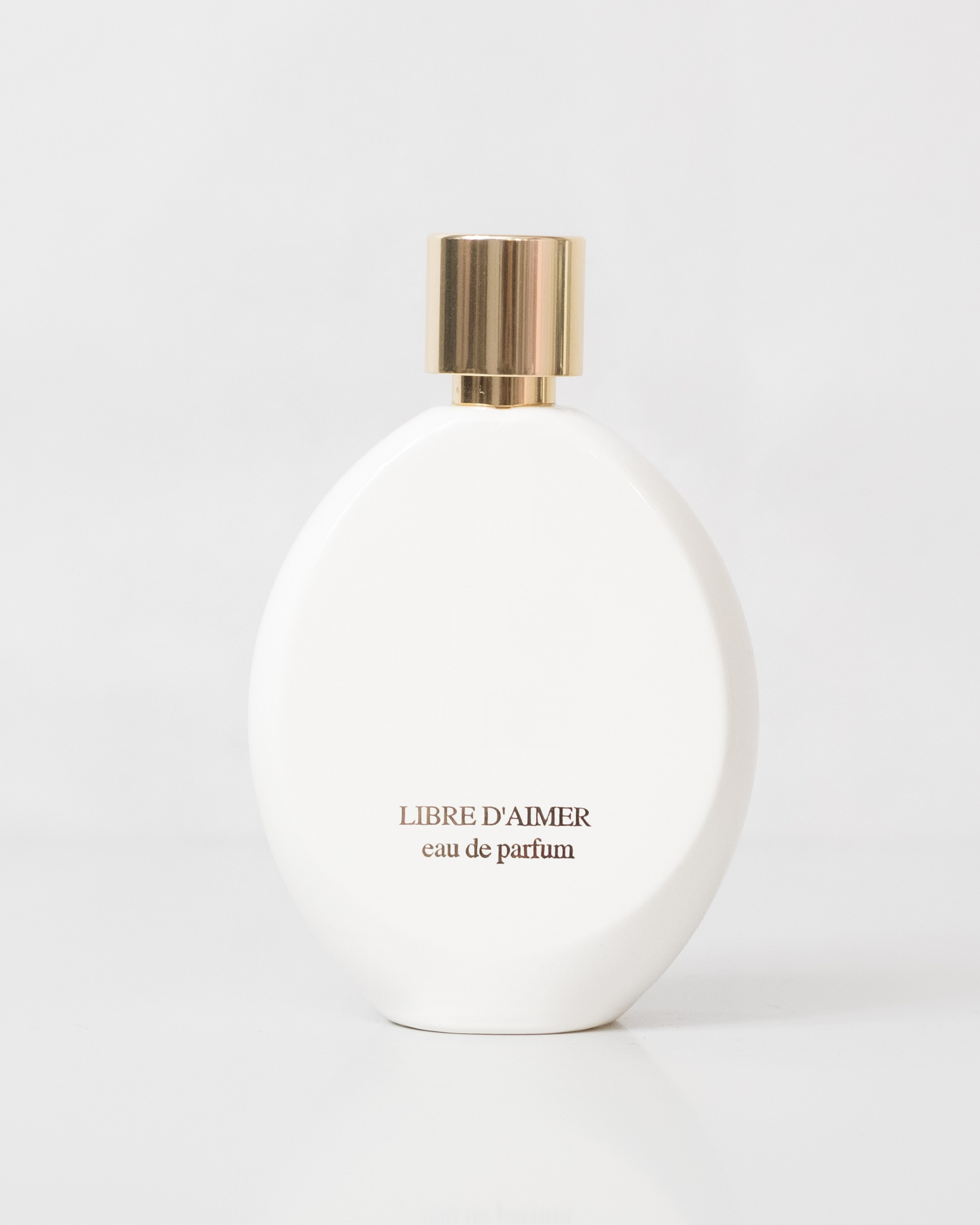 Minimalist white perfume bottle with a gold cap on a light background