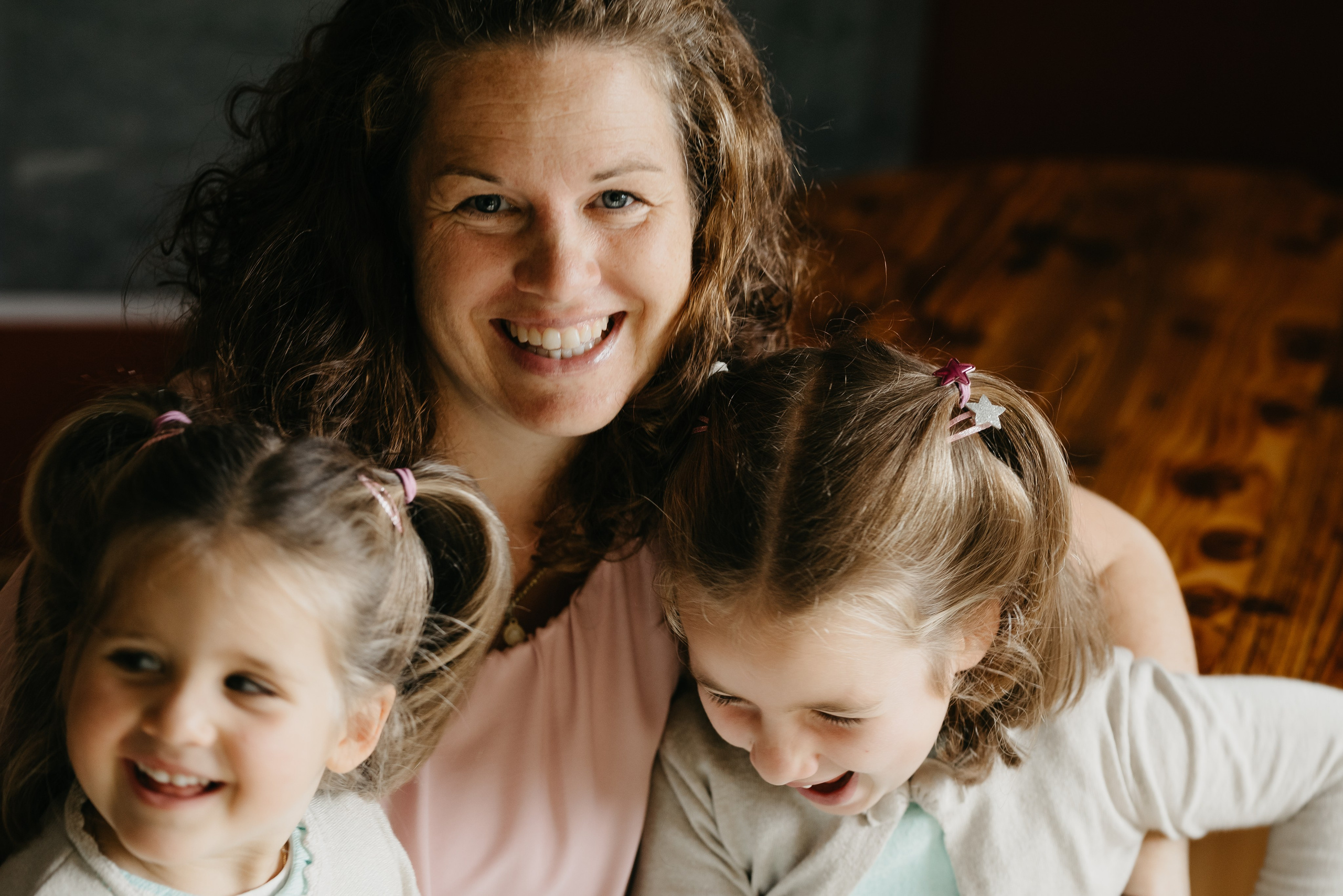 eine lächelnde Mutter und ihre beiden kleinen Töchter die sich umarmen