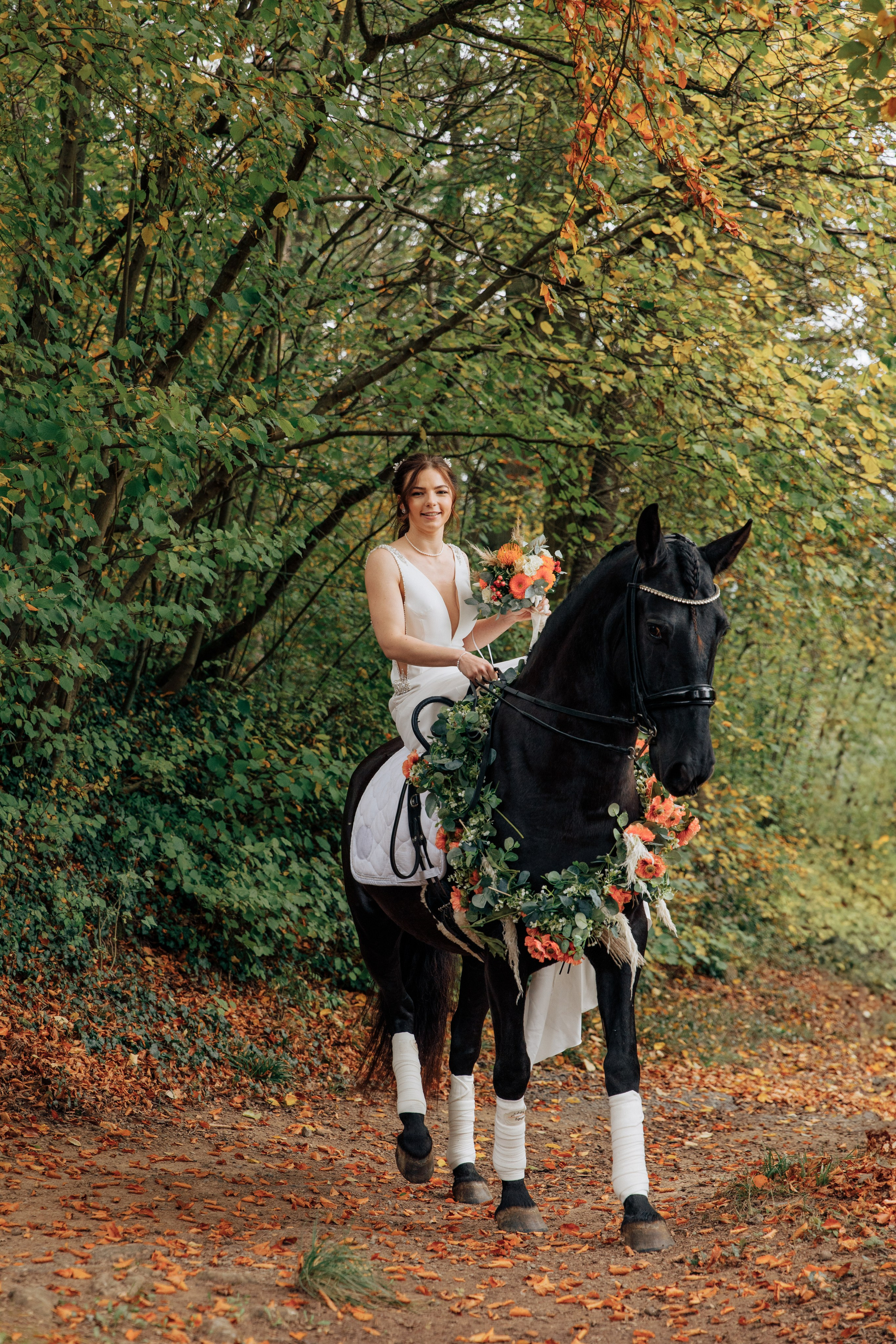 Die Braut sitzt auf einem dunklen Pferd, schaut nach vorne und lächelt, in einer Hand hält sie den Hochzeitsstrauß.