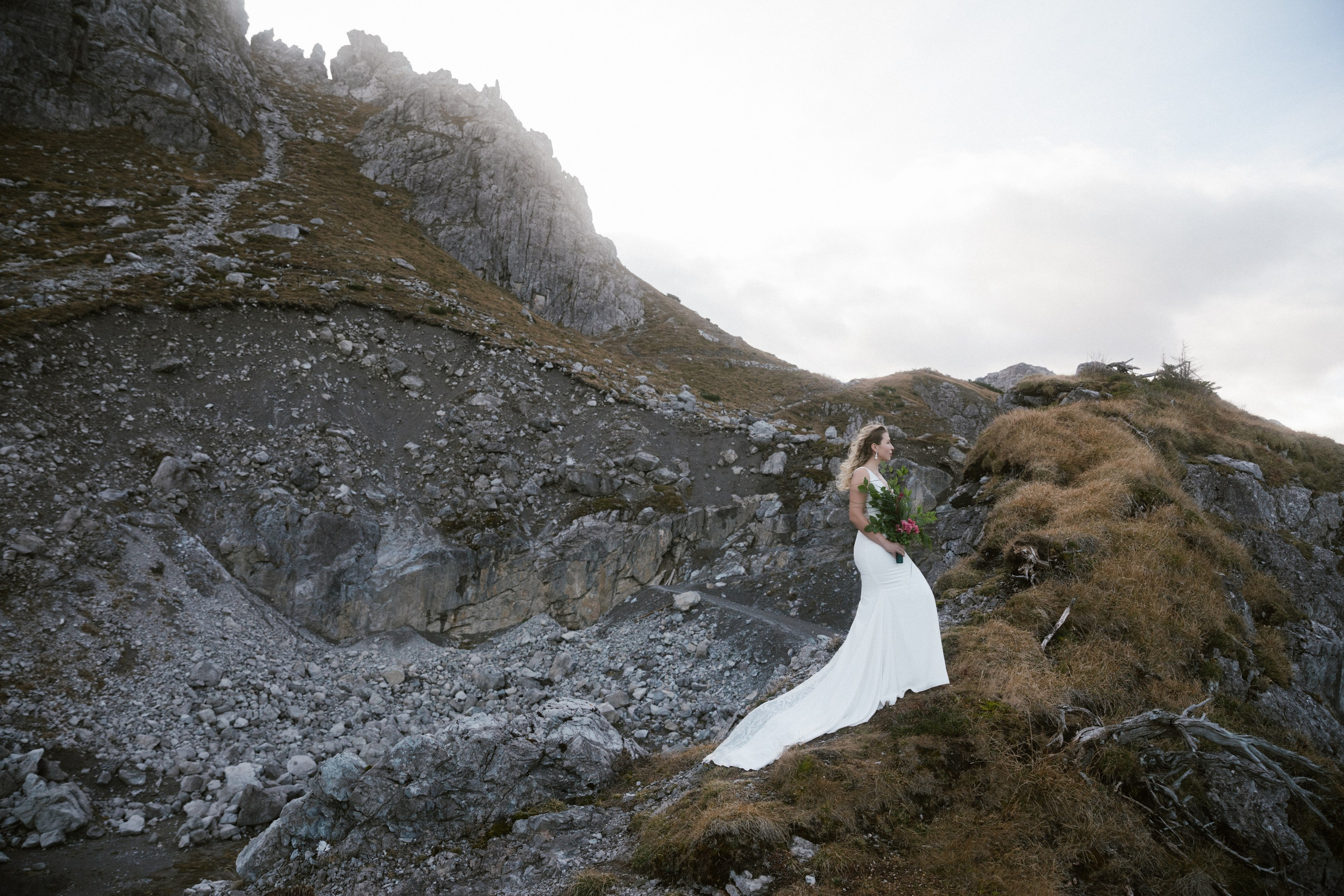Braut im weißen Kleid mit Strauß auf alpinem Fels bei Hochzeitsfotos