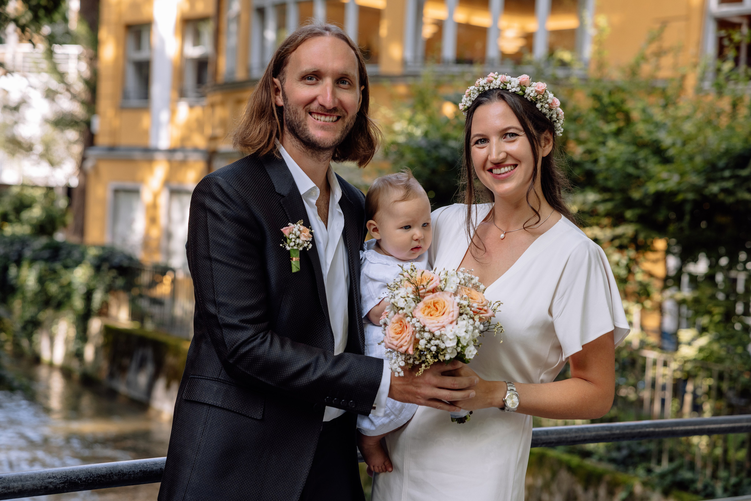 Detailaufnahme – Hände der Eltern halten Baby sanft, Trausaal im Hintergrund