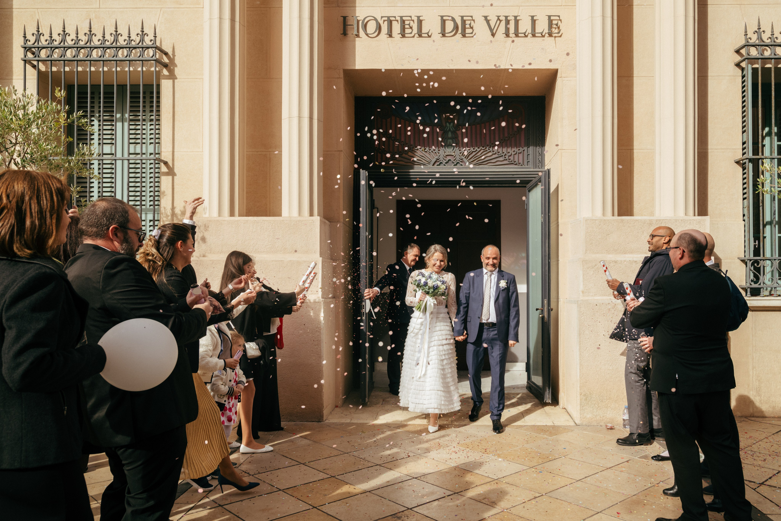 Молодожёны выходят из мэрии, а гости осыпают их конфетти.