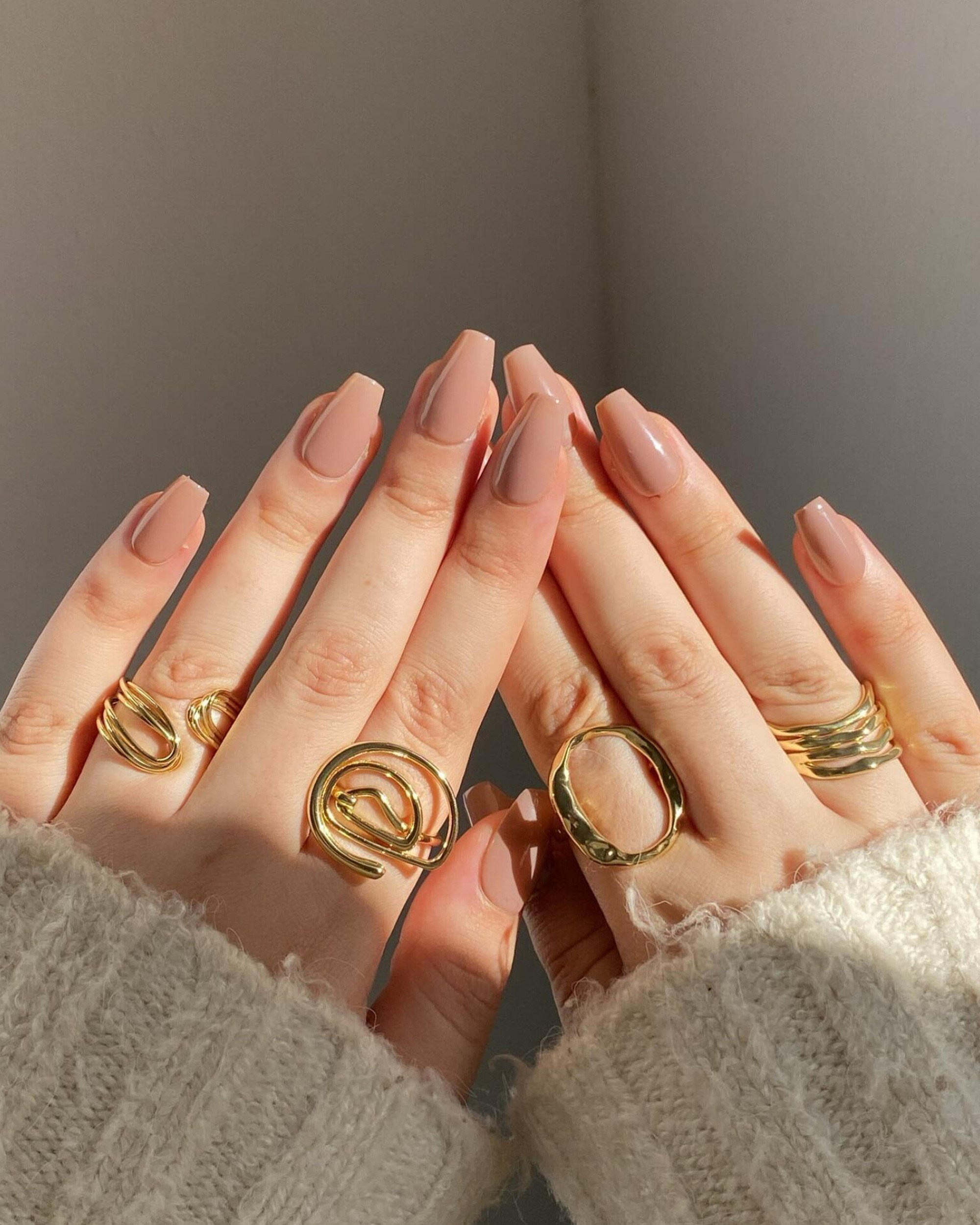 Fashionable display of gold rings on hands with a neutral manicure, bathed in natural light