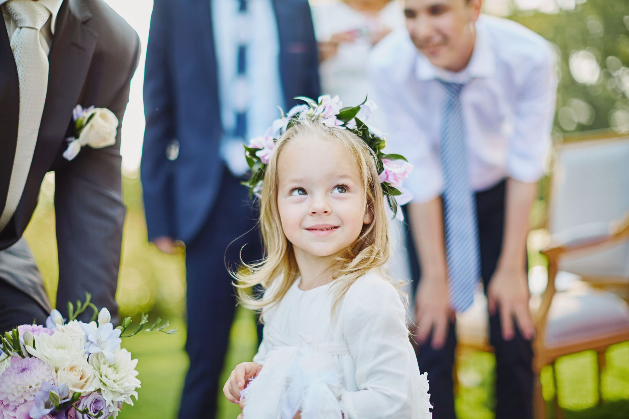 Cute flower girl with floral headpiece seeking mother's approval at wedding.