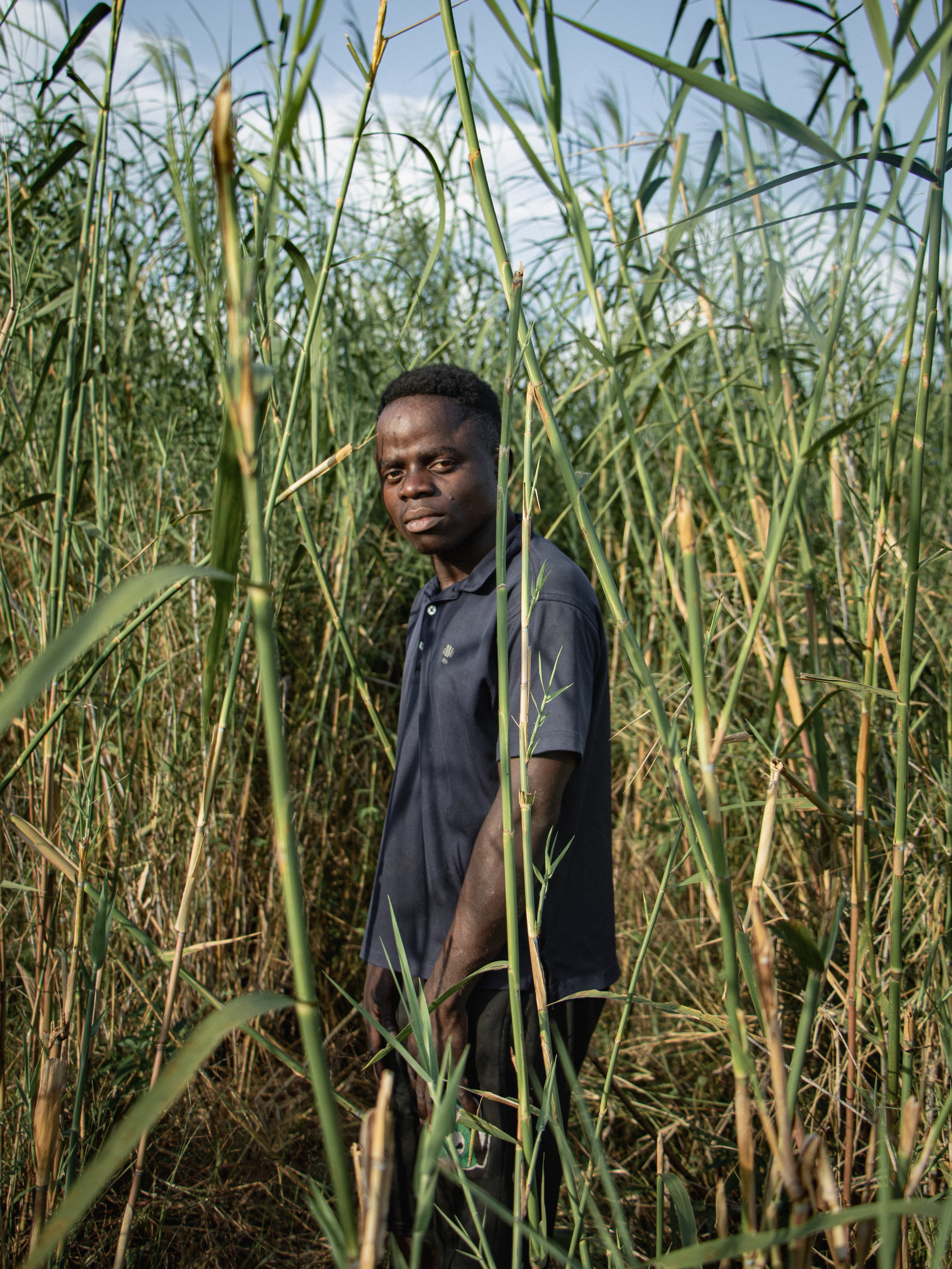 Un jeune habitant se tient entre les roseaux, à quelques pas du fleuve Zambèze, sur les terres agricoles transmises par ses ancêtres.Comme de nombreux jeunes de la région, il grandit dans l’incertitude. Le projet de méga barrage de Mphanda Nkuwa plane comme une menace silencieuse : à tout moment, les autorités pourraient ordonner l’expulsion des familles pour faire place au chantier.