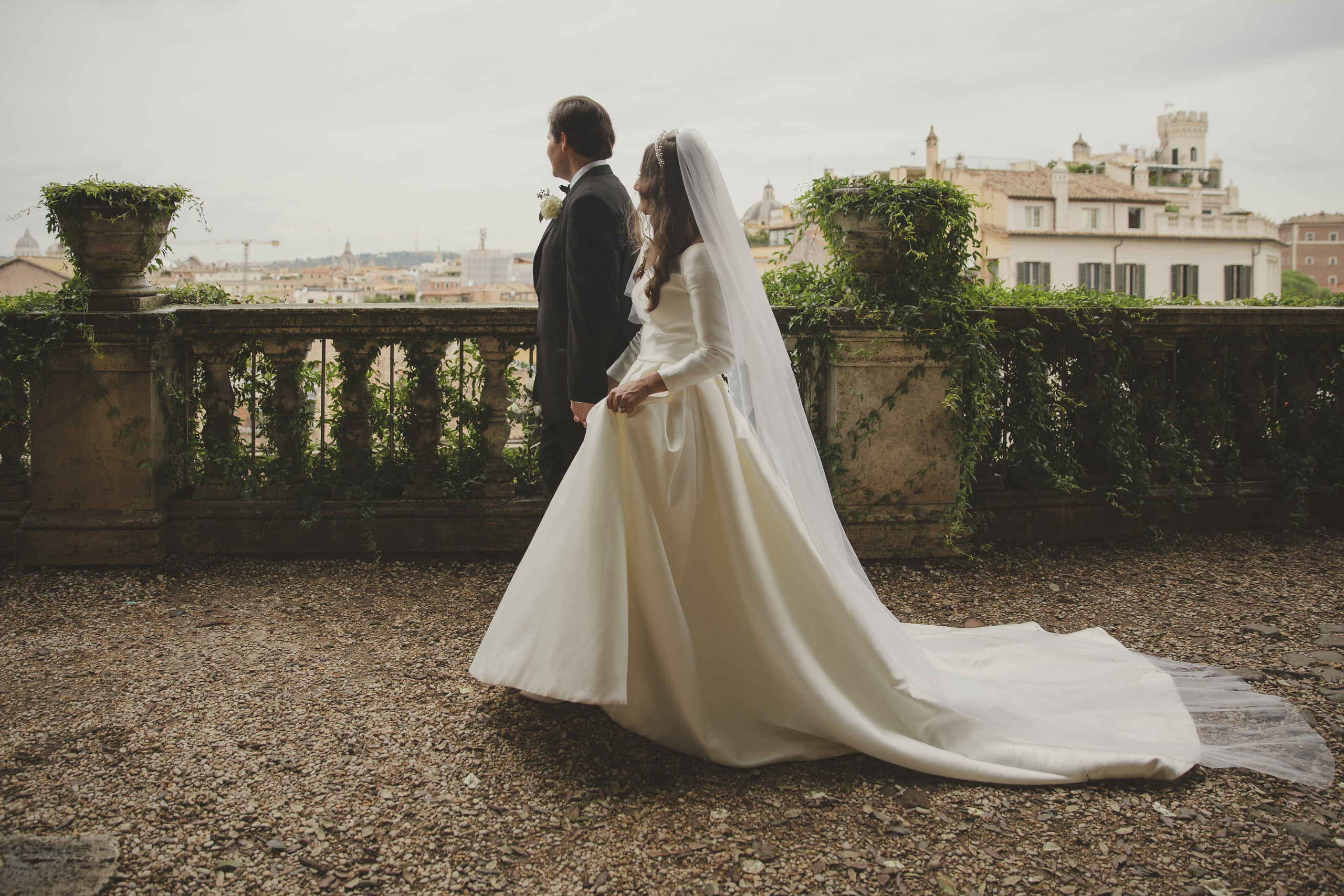 Newly married couple walking hand-in-hand through a beautiful luxury garden in Rome.