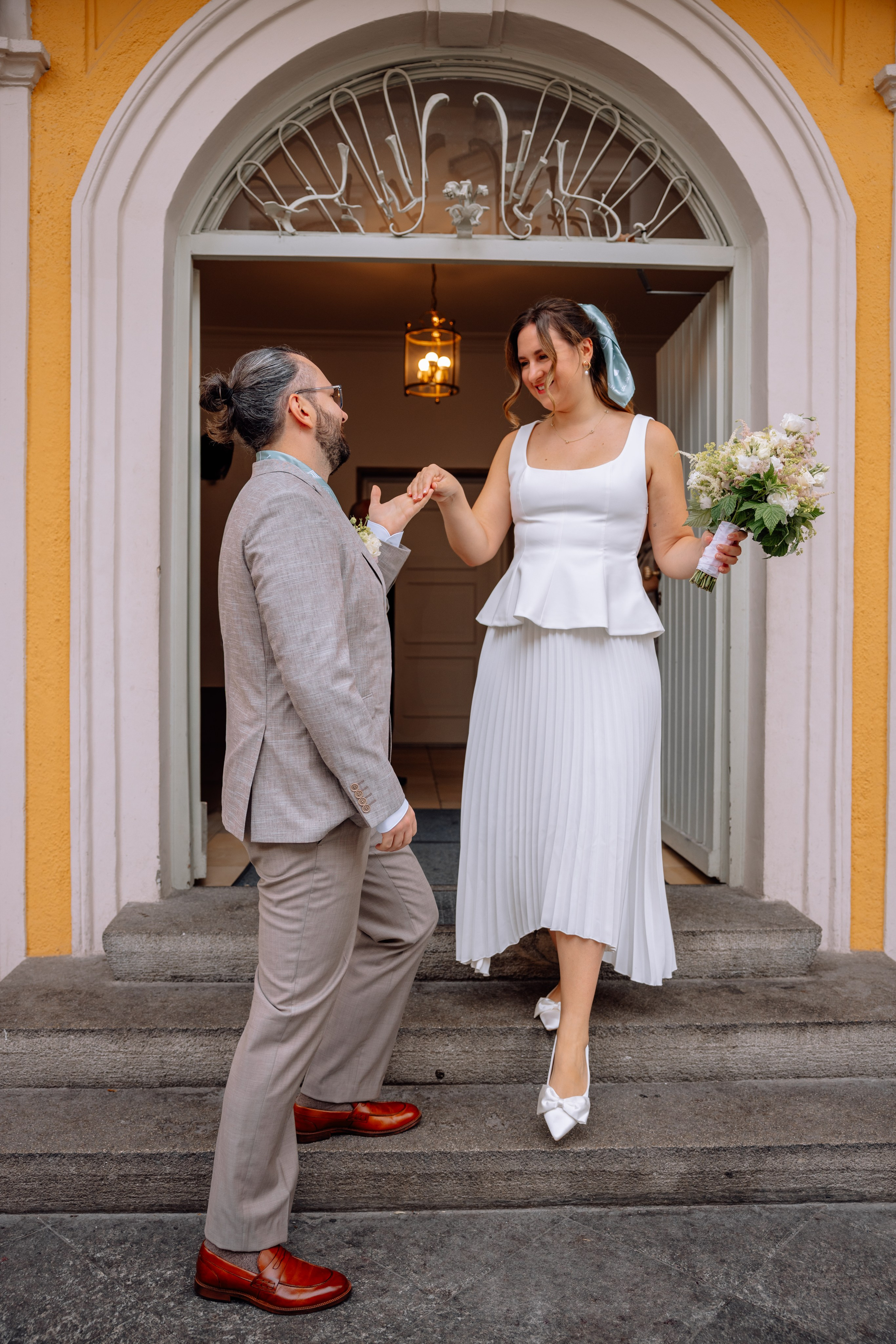 Bräutigam hält Braut an der Hand – hilft ihr die Treppe des Standesamts hinunter.