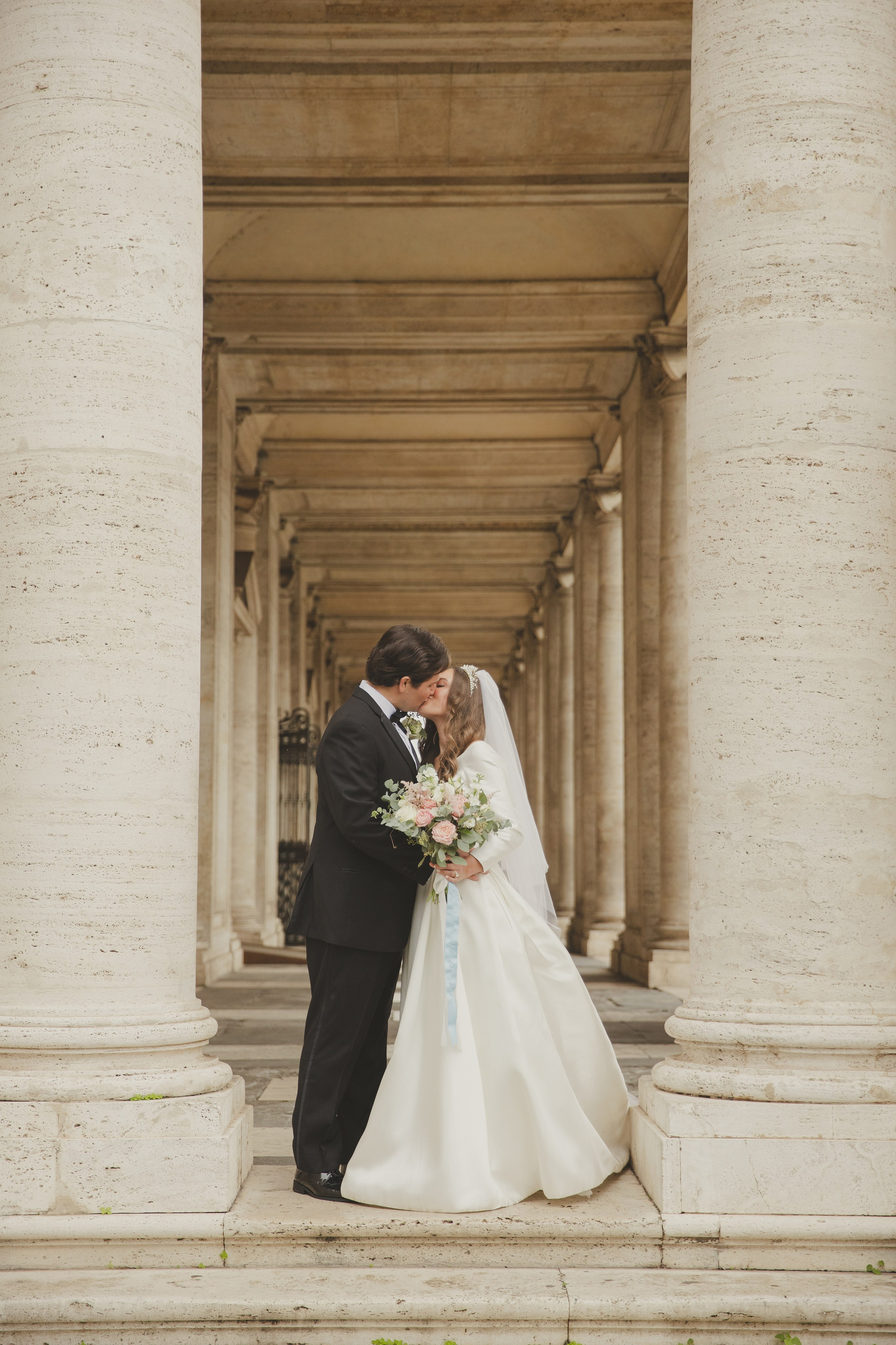 A newly married couple sharing a kiss in the arcades of Piazza del Campidoglio.