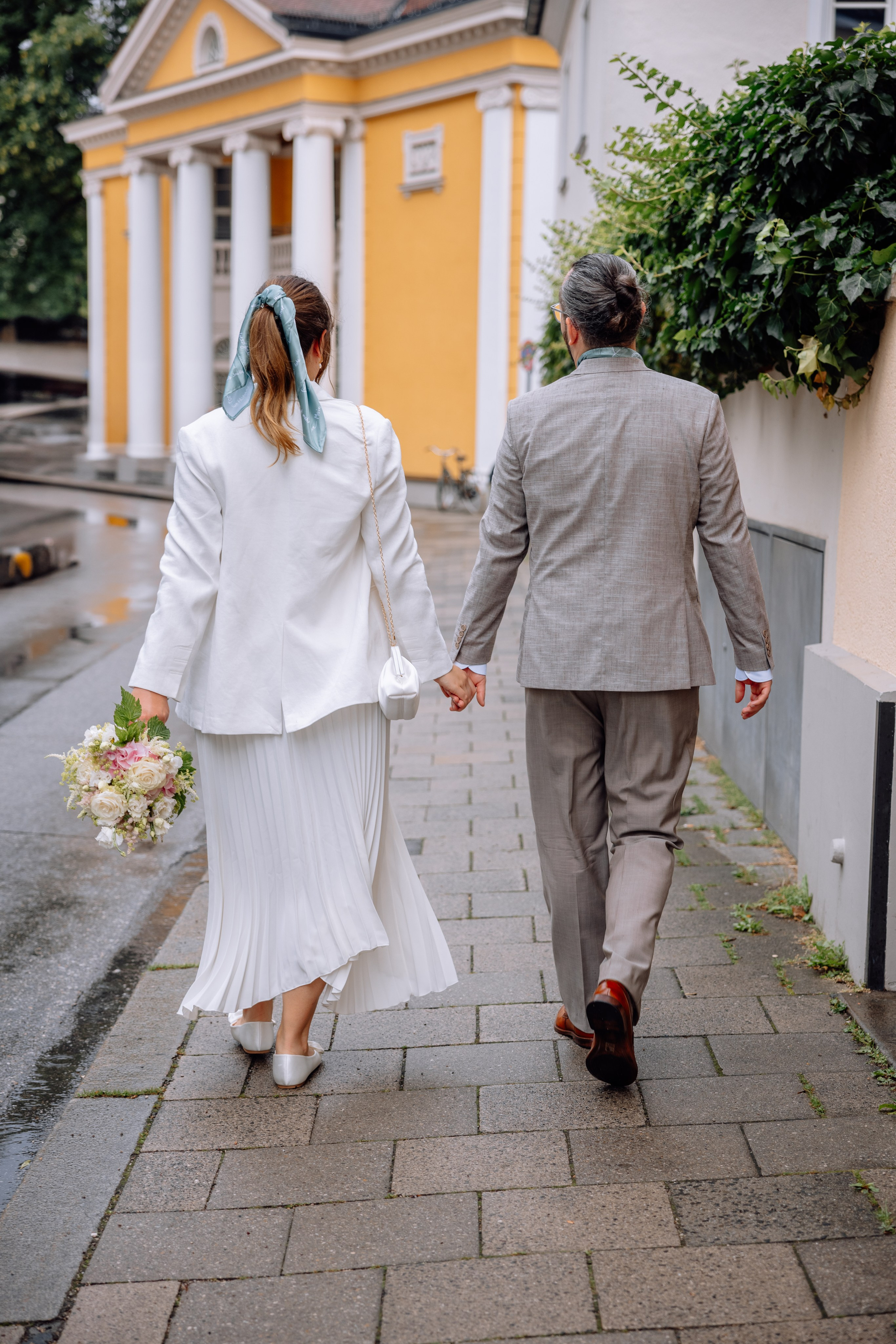 Braut und Bräutigam halten sich an den Händen – Standesamt Mandlstraße 14 im Hintergrund