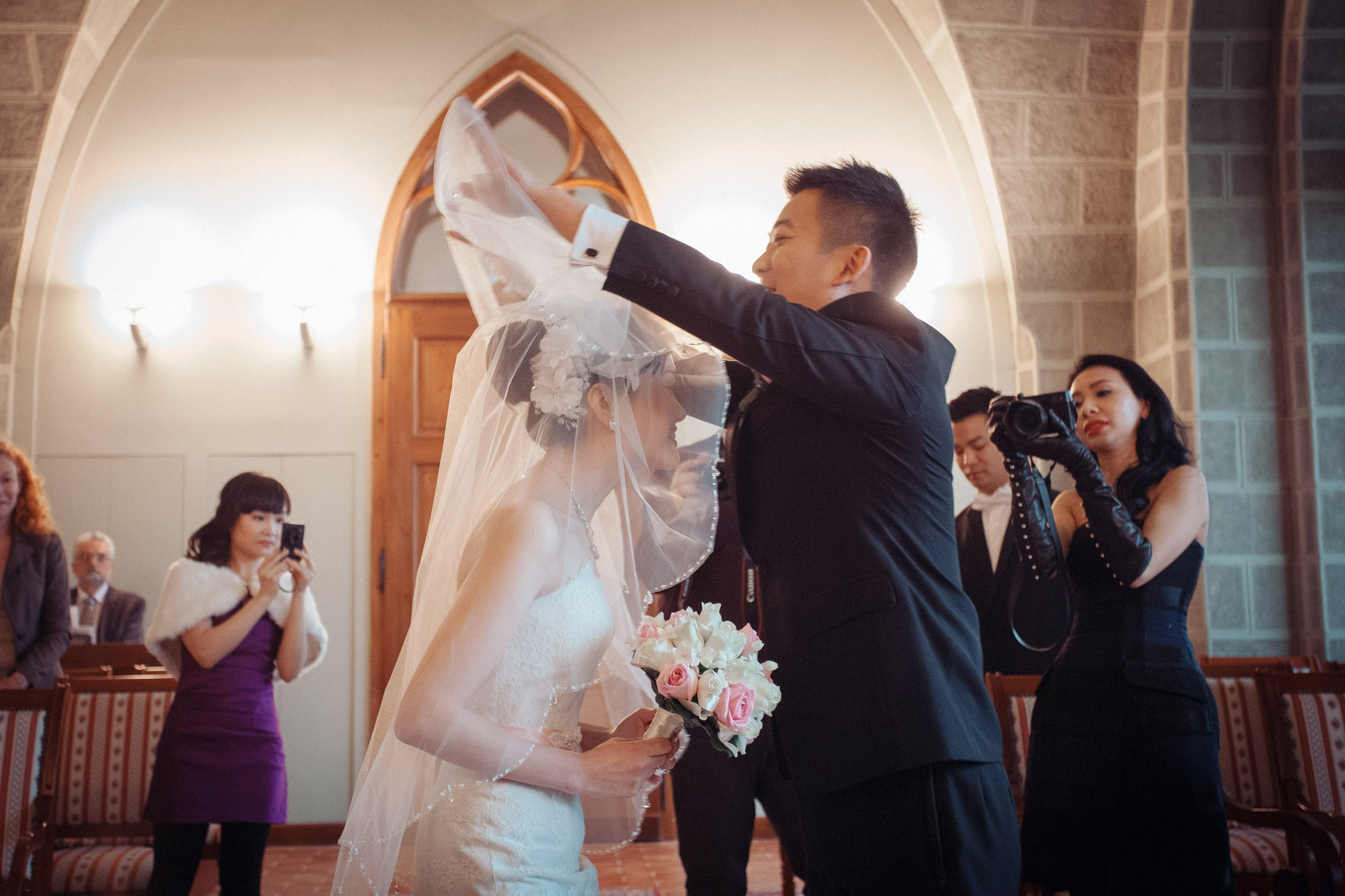 A Hong Kong groom enveils his bride as ther family & friends take pictures of their wedding at the Castle Hluboka in Czechia.