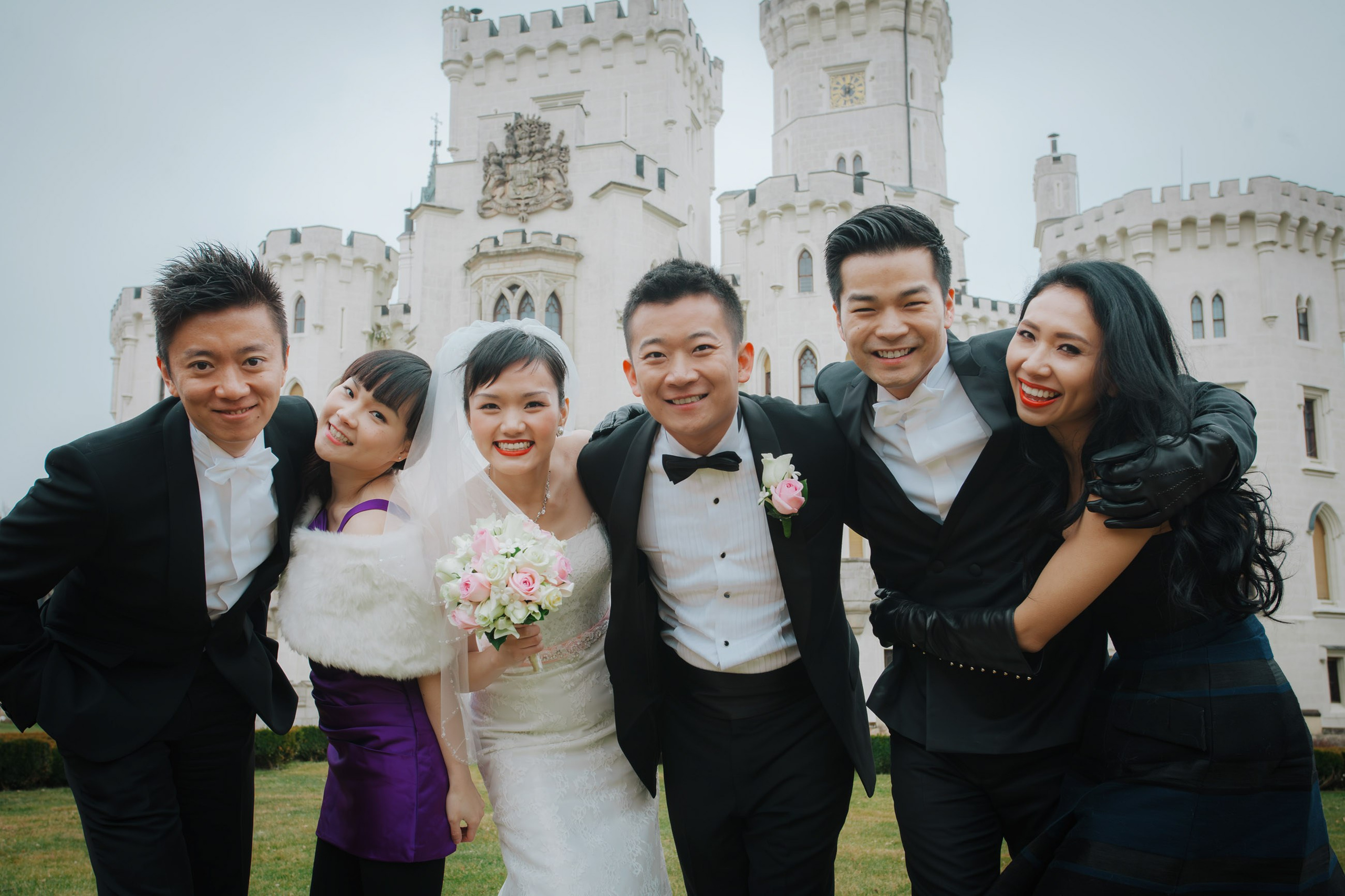 A groud photo of smartly dressed young people from Hong Kong as they pose for a photo with the newlyweds on the grounds of the State Chateau of Hluboka.