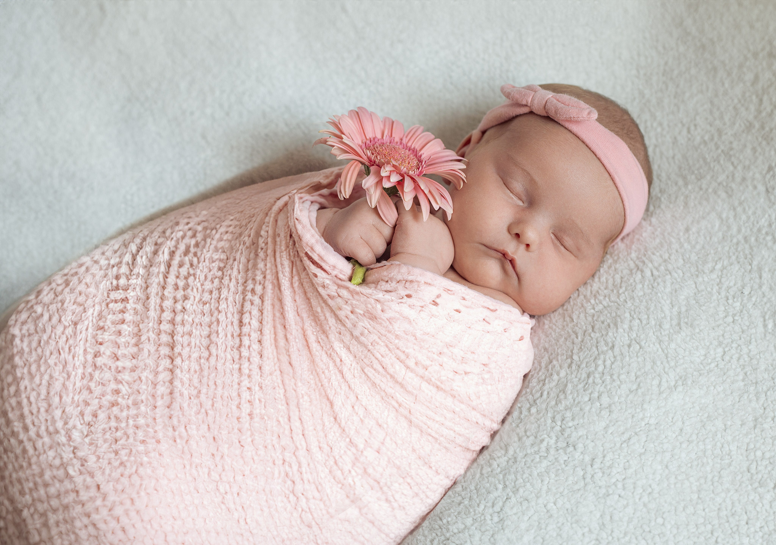Portrait de bébé fille emmaillotée en rose avec bandeau et fleur, photo de naissance délicate