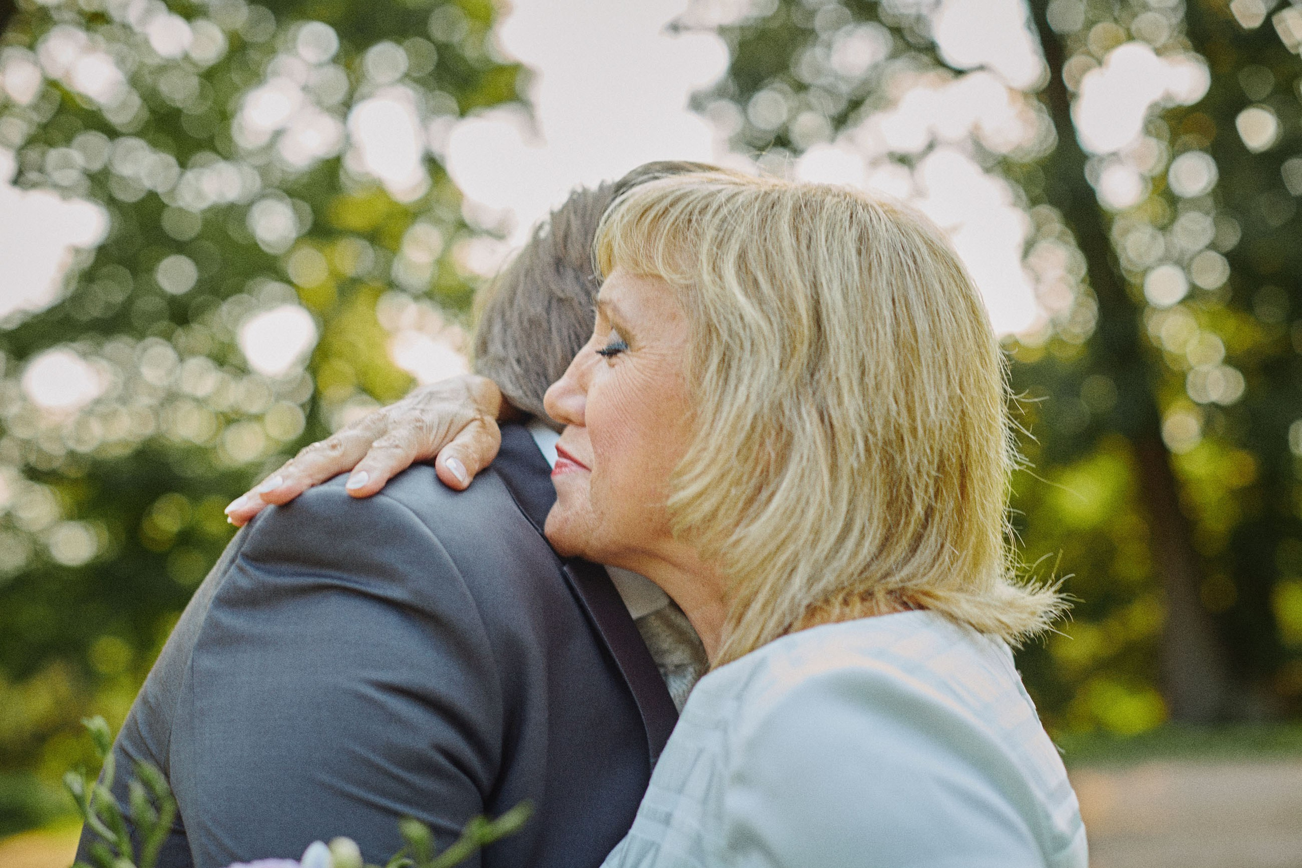 Groom embraced by mother after outdoor chateau wedding
