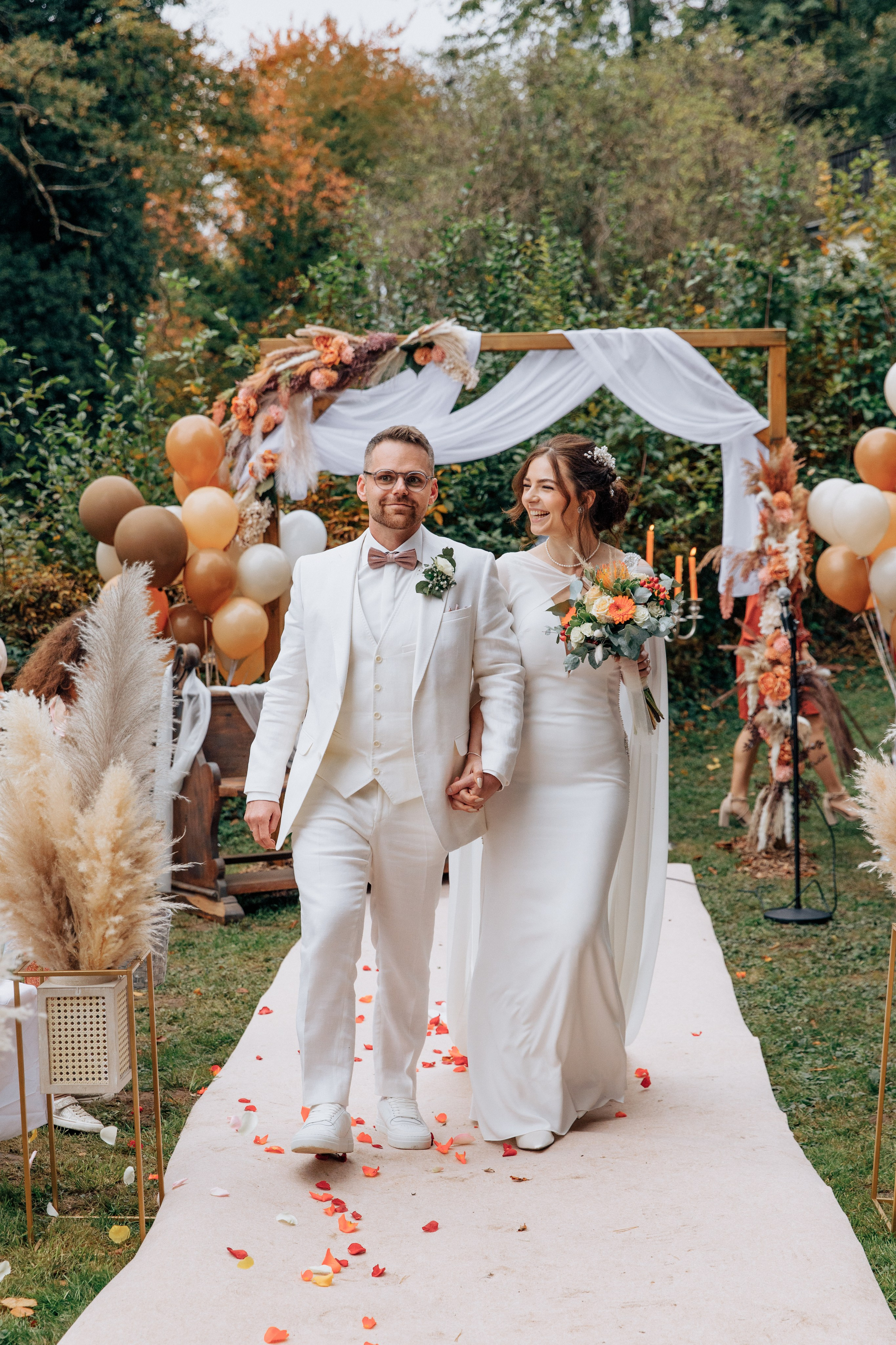 Der Bräutigam und die Braut gehen den weißen Gang entlang, der mit Blütenblättern bedeckt ist.