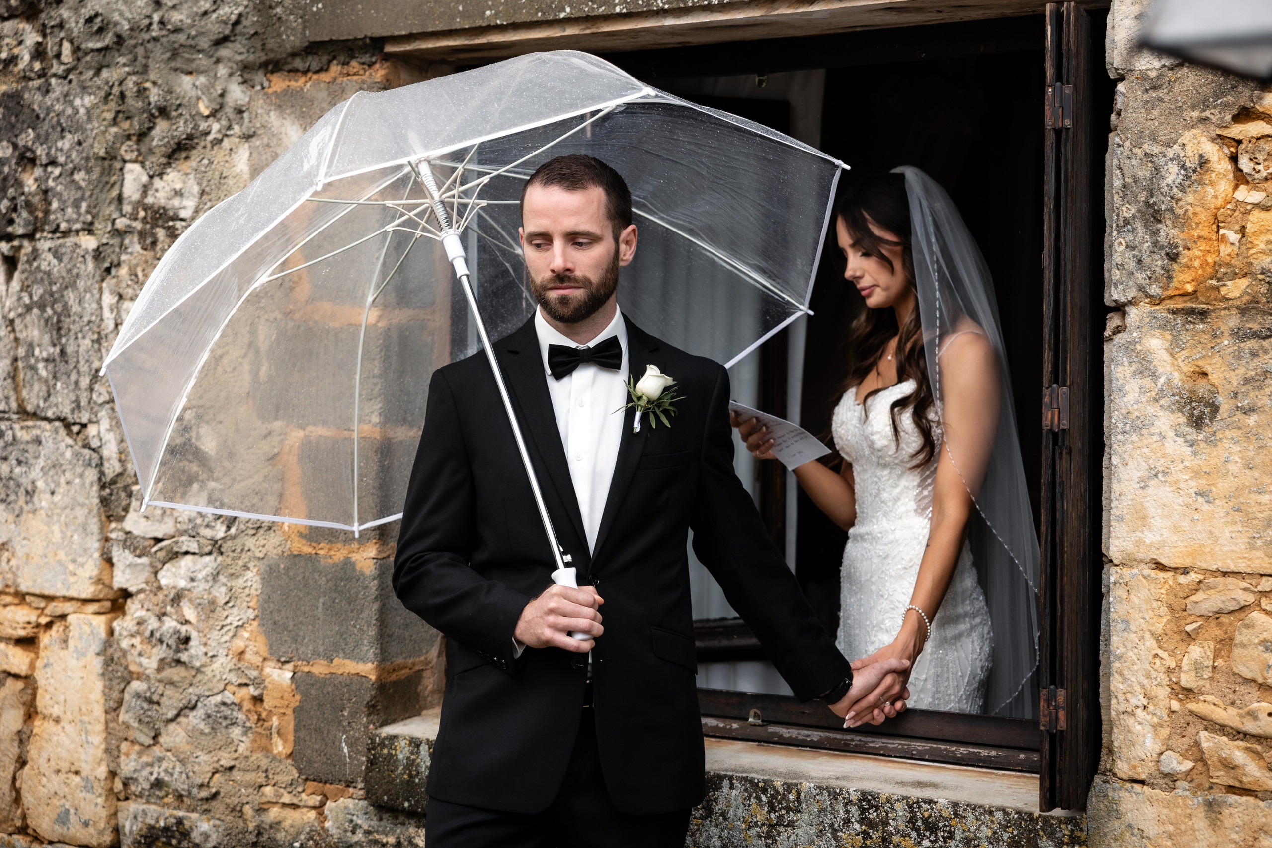 Groom standing under umbrella during rainy wedding in Dordogne, France.