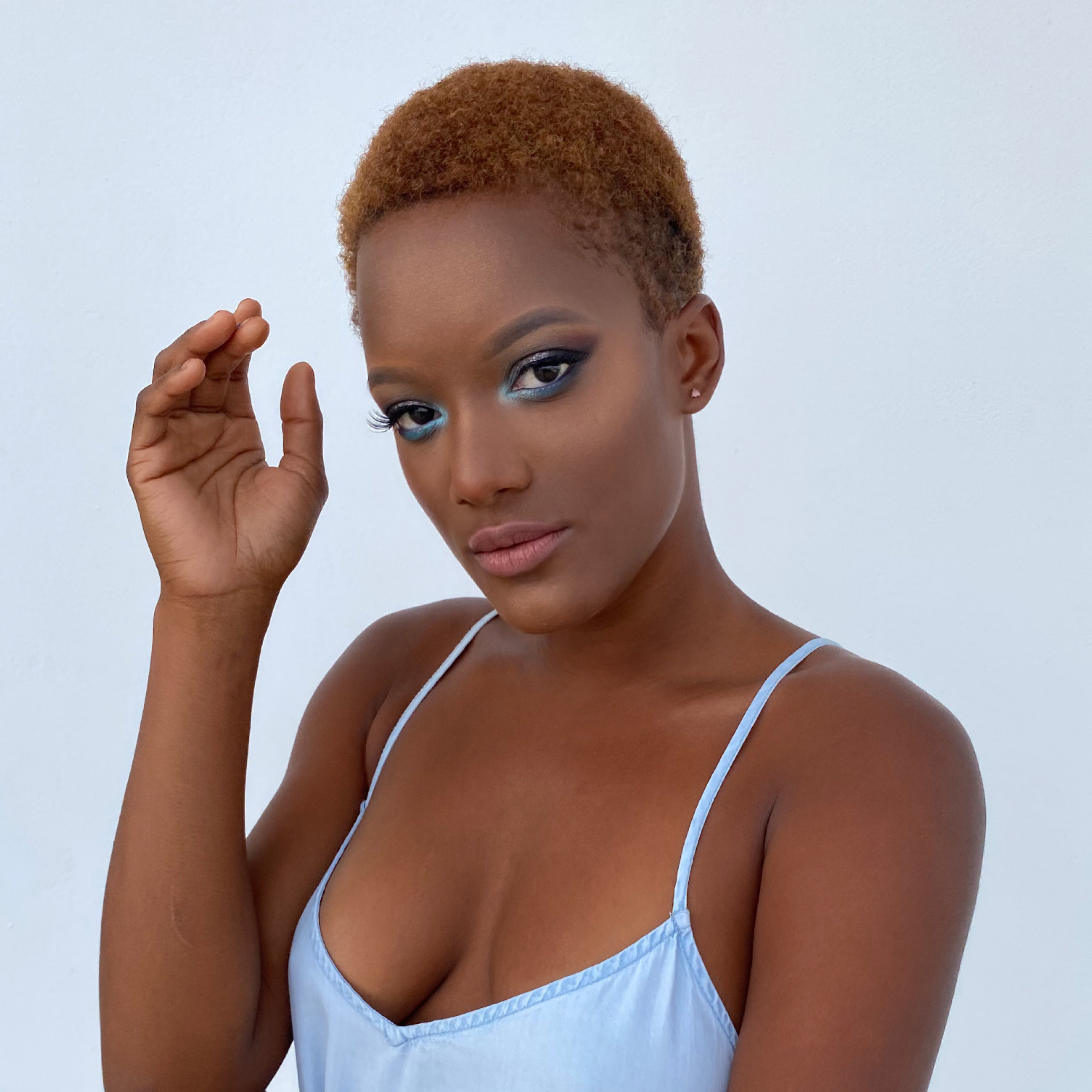 a dark skin woman with bright blue cat eye makeup in a light blue jeans dress