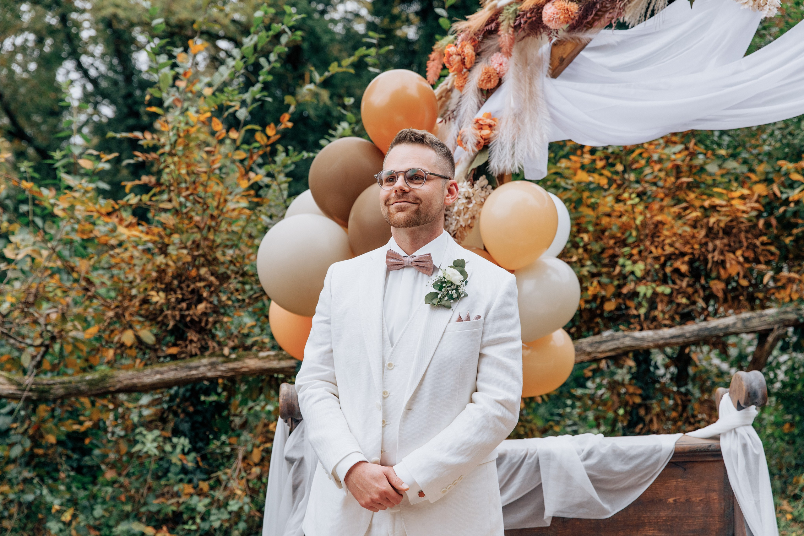 Der Bräutigam schaut die Braut an und lächelt, im Hintergrund ist eine schöne herbstliche Dekoration.