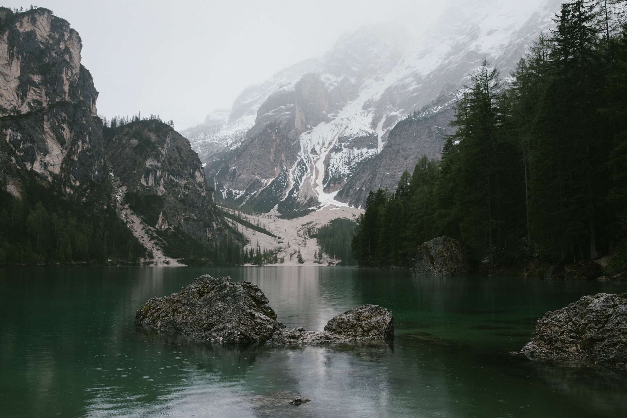 Nebliger Bergsee mit smaragdgrünem Wasser und felsigem Ufer