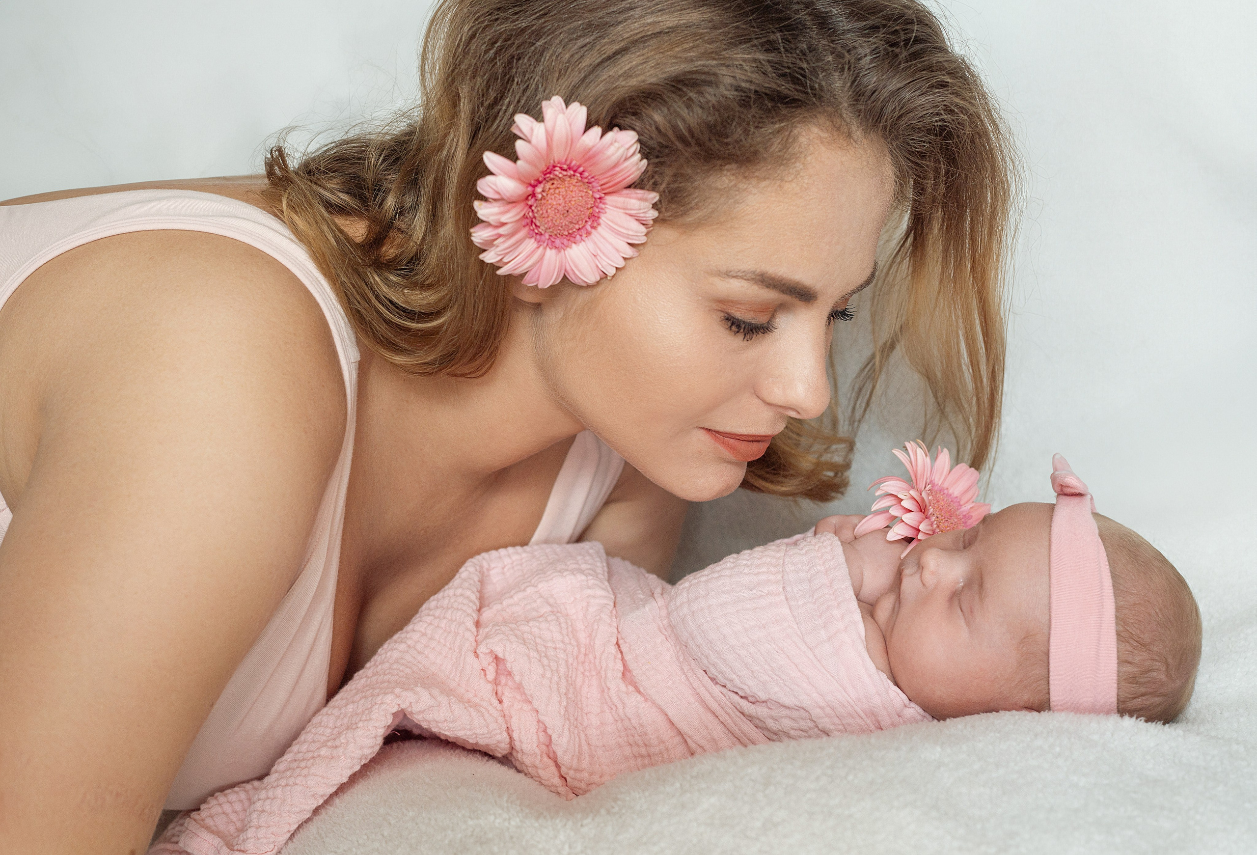 Maman regarde tendrement son nouveau-né, séance photo naissance en rose pastel avec fleur