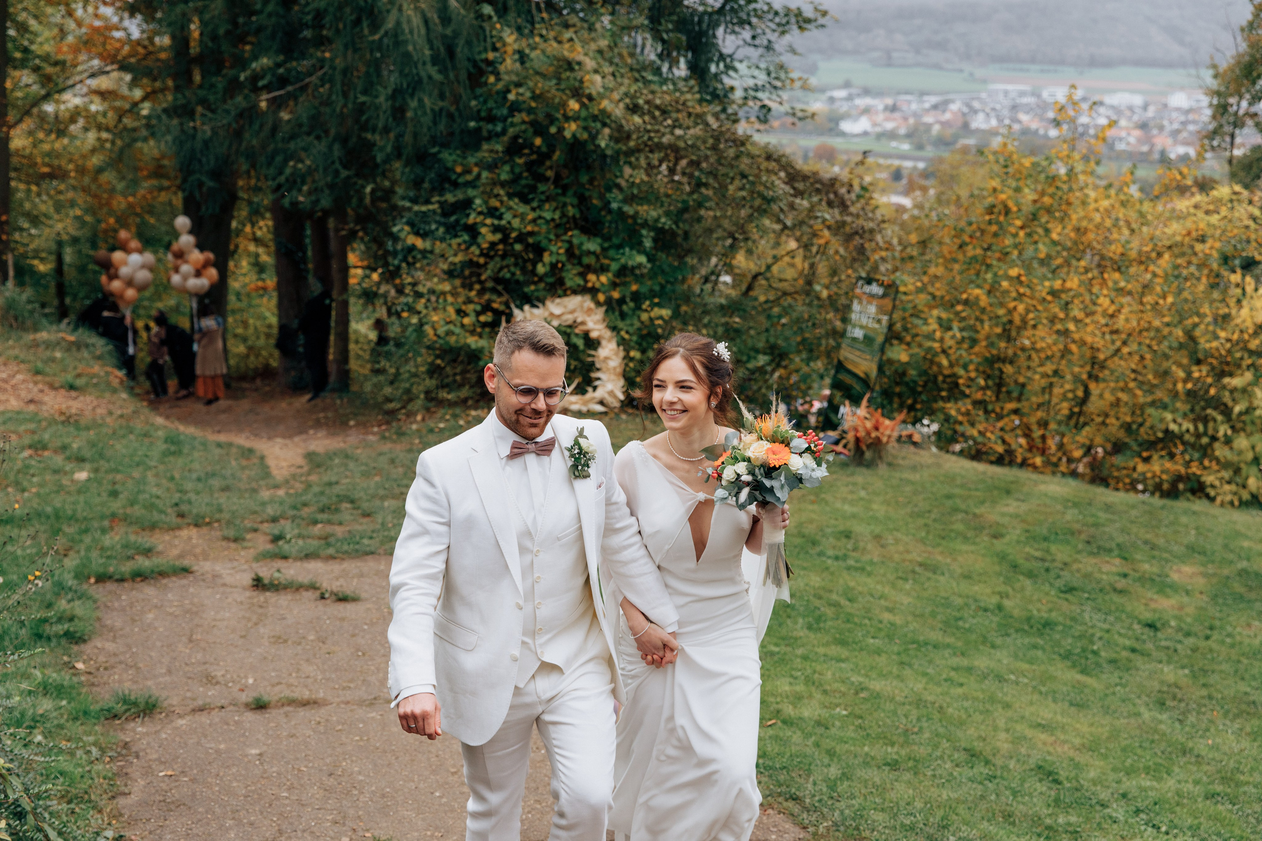 Der Bräutigam und die Braut steigen den Hügel hinauf und lächeln, im Hintergrund öffnet sich eine schöne Aussicht.