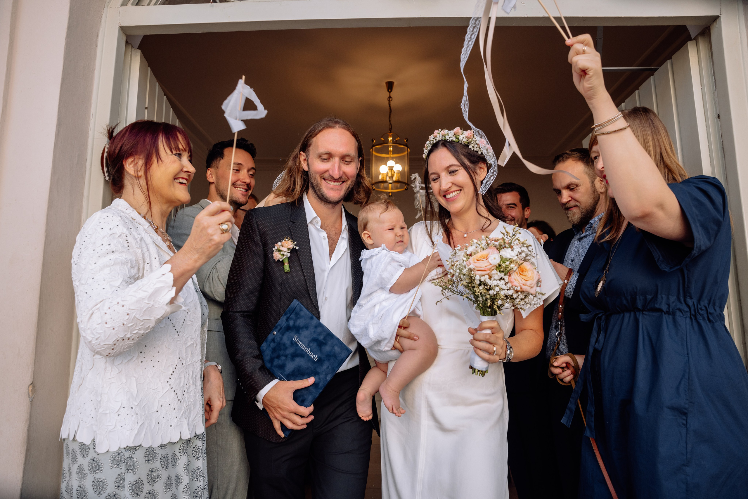 Brautpaar verlässt das Standesamt Schwabing Mandlstraße 14 – glückliche Familie mit Baby, Gäste schwenken weiße Bänder